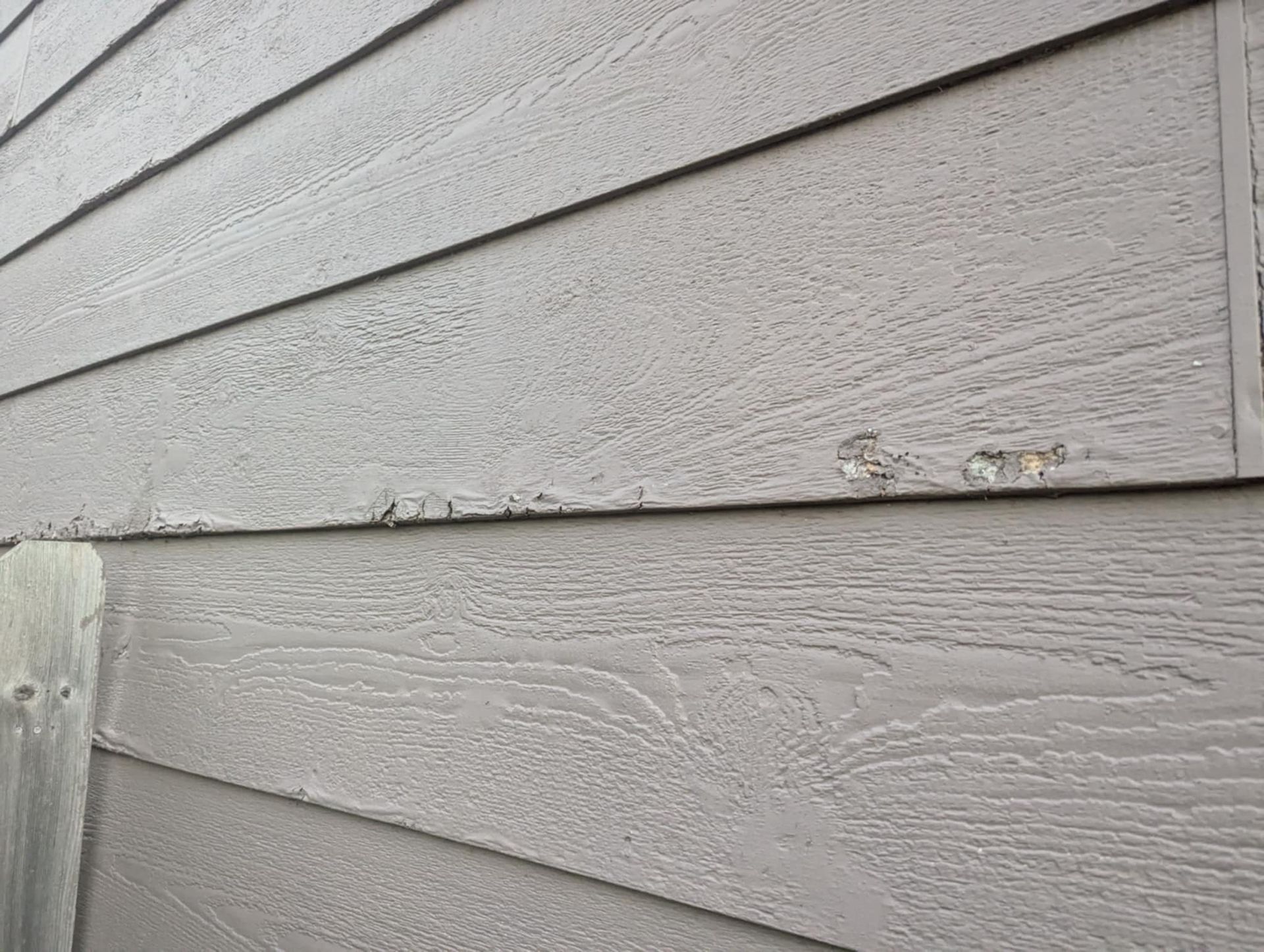 Gray siding on a building with some damaged areas and wood-grain texture.