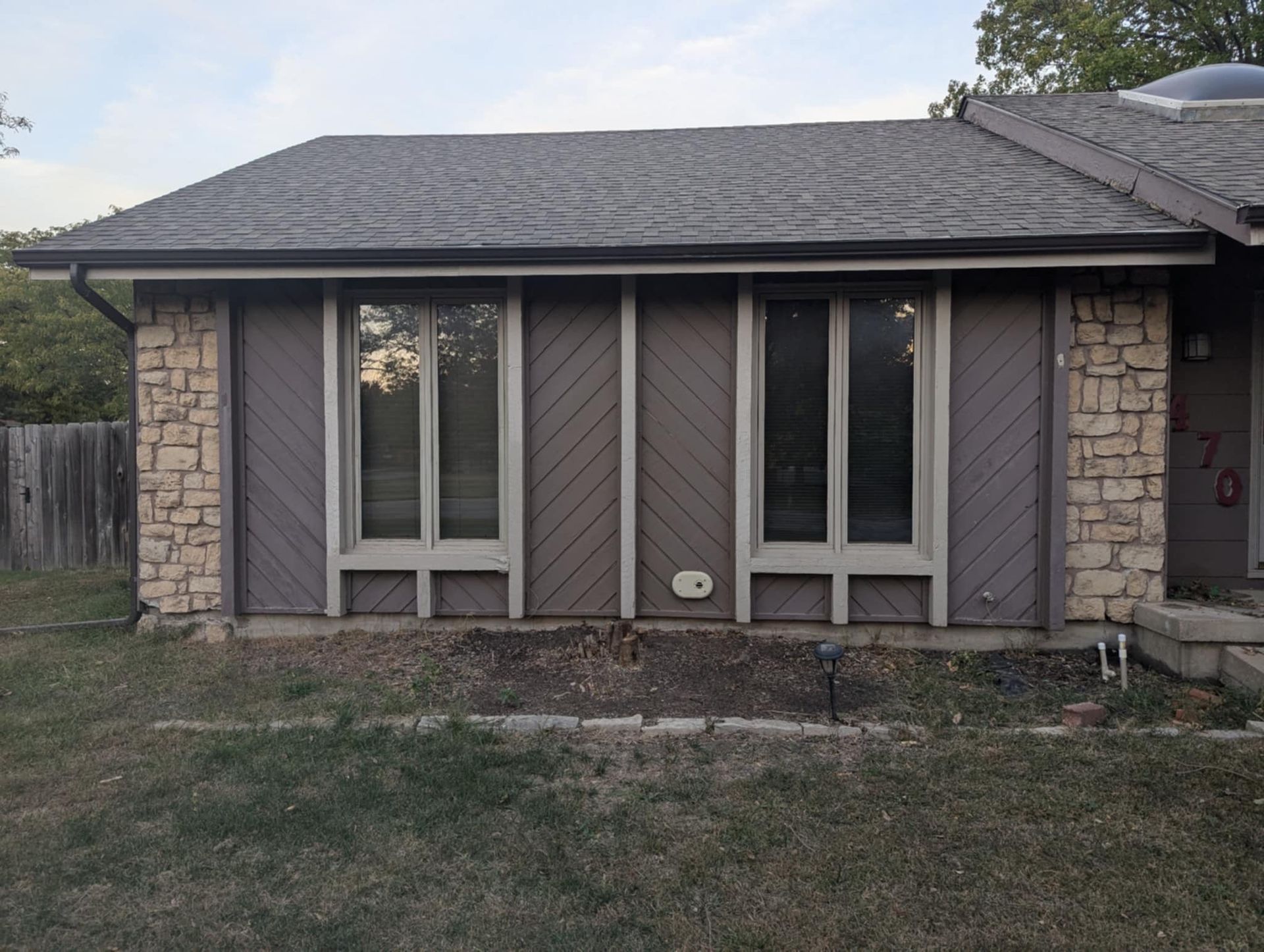 Brown house with stone accents, two windows, and a gray roof.