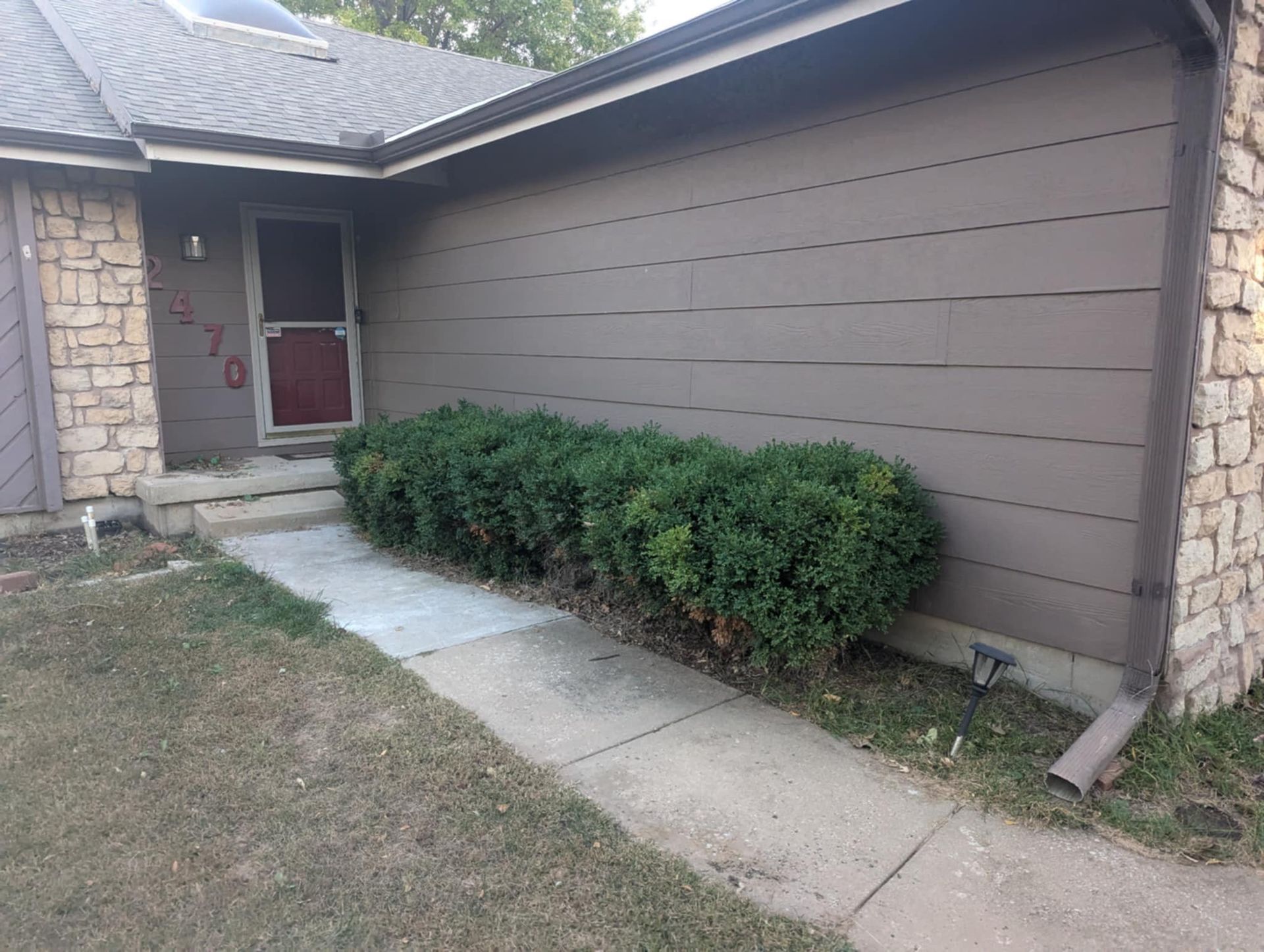 Brown house with walkway, bushes, and stone accents.
