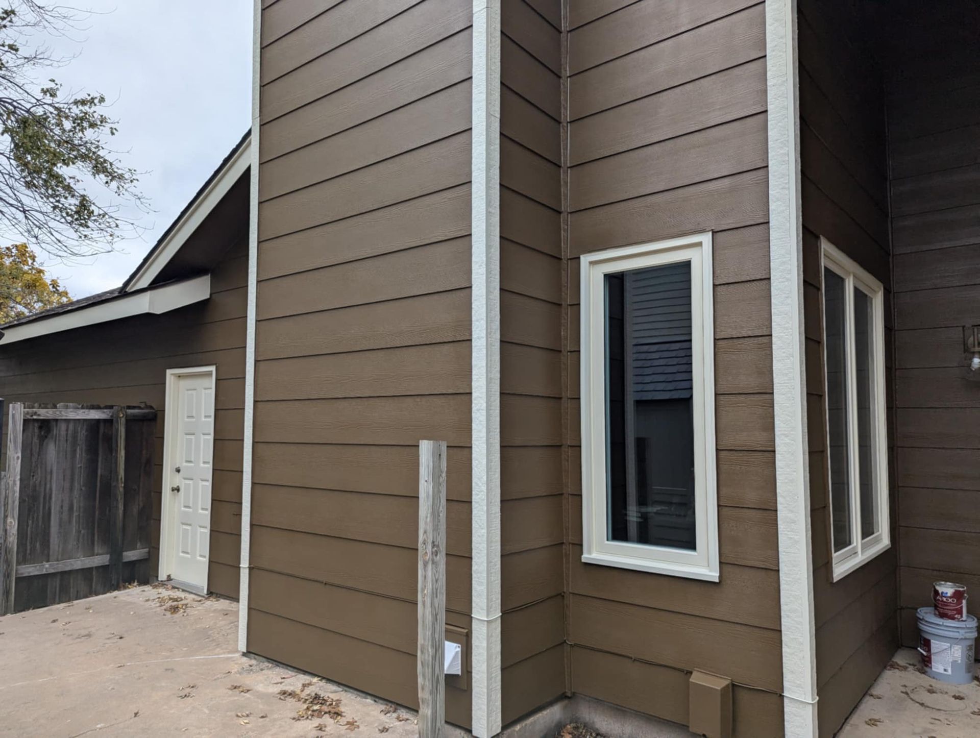 Brown house exterior with white trim and windows on a cloudy day.