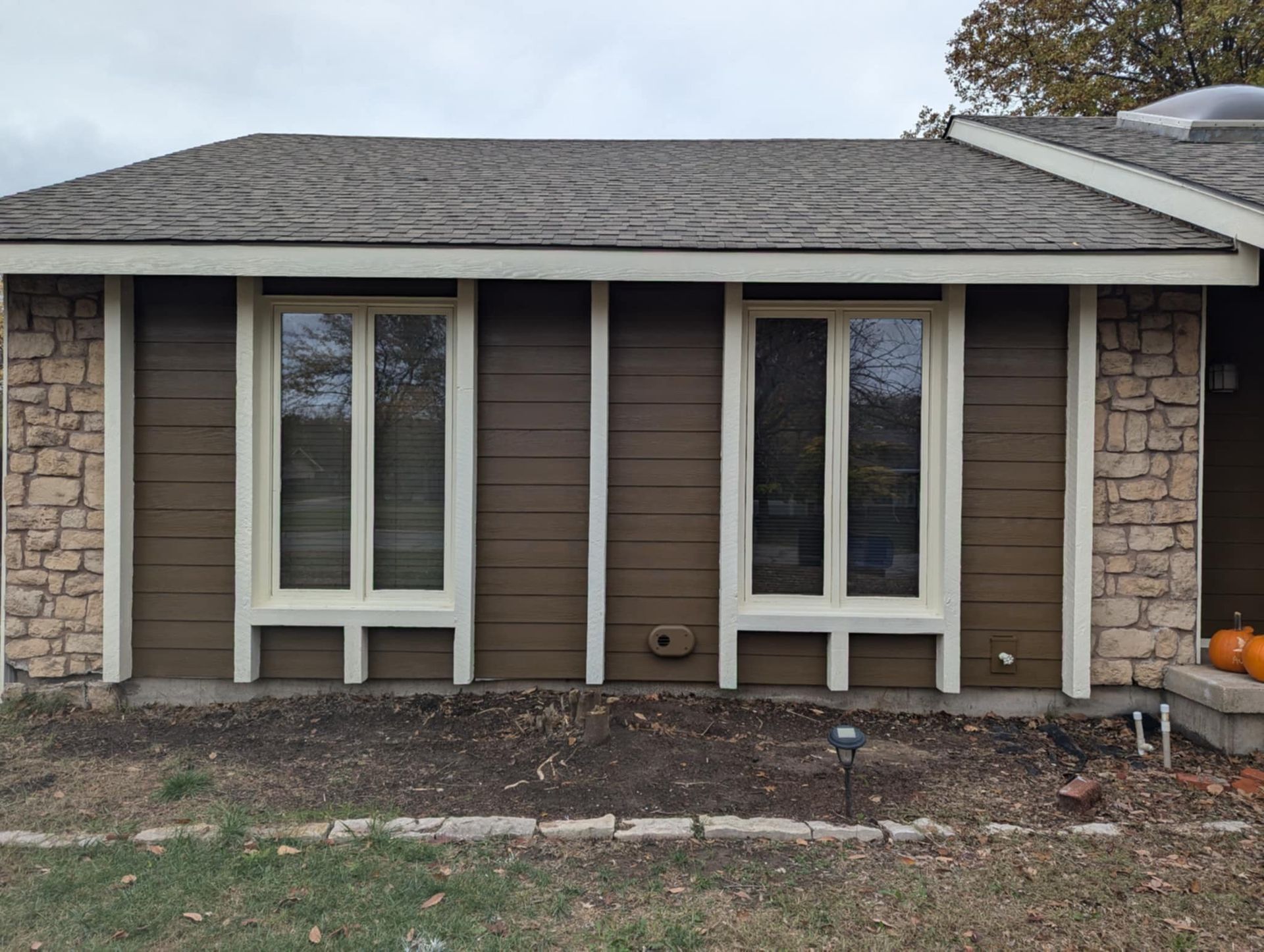 Brown house exterior with two windows, tan trim, stone accents, and a brown roof.