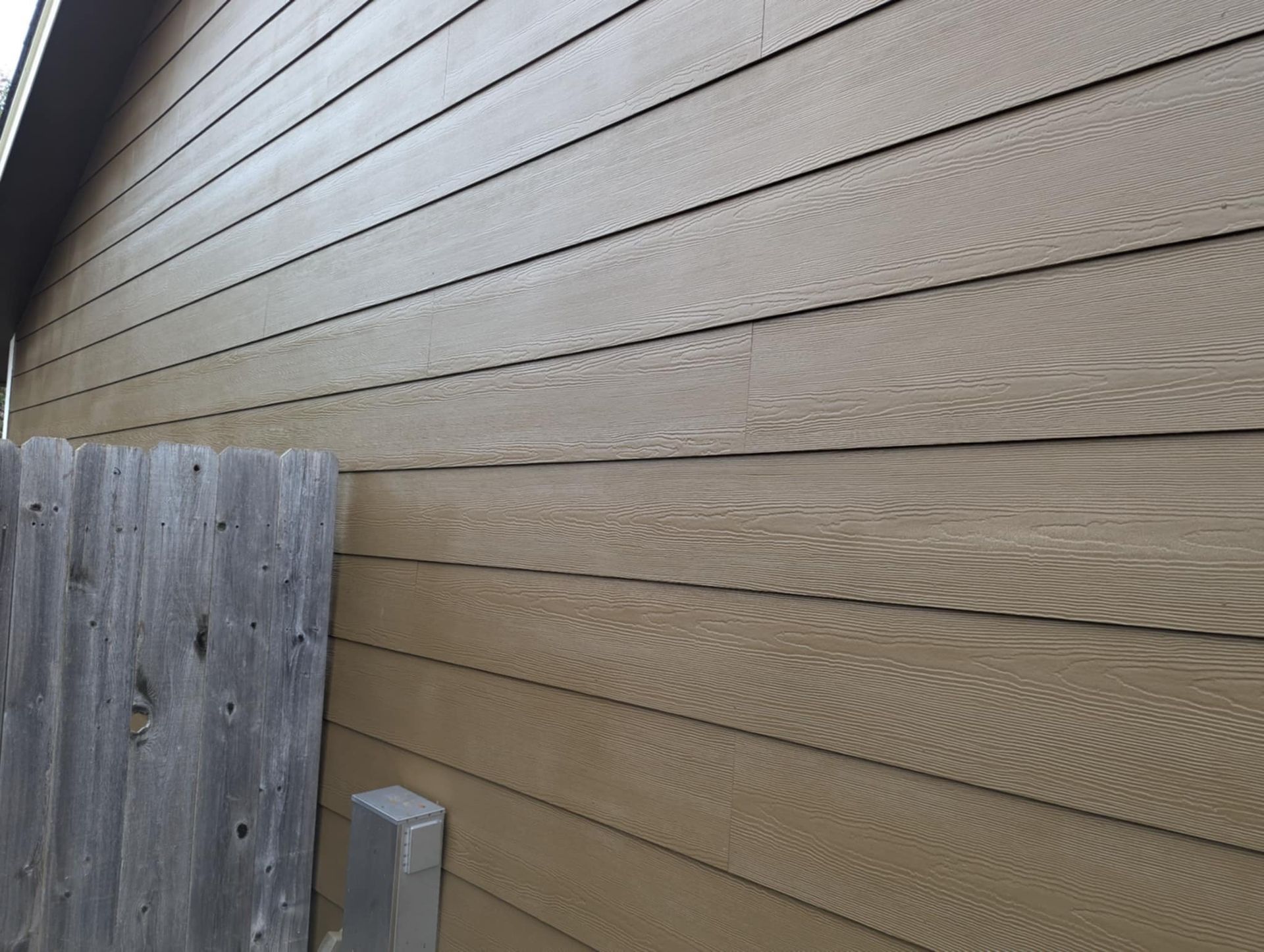 Brown siding on a house next to a weathered wooden fence.