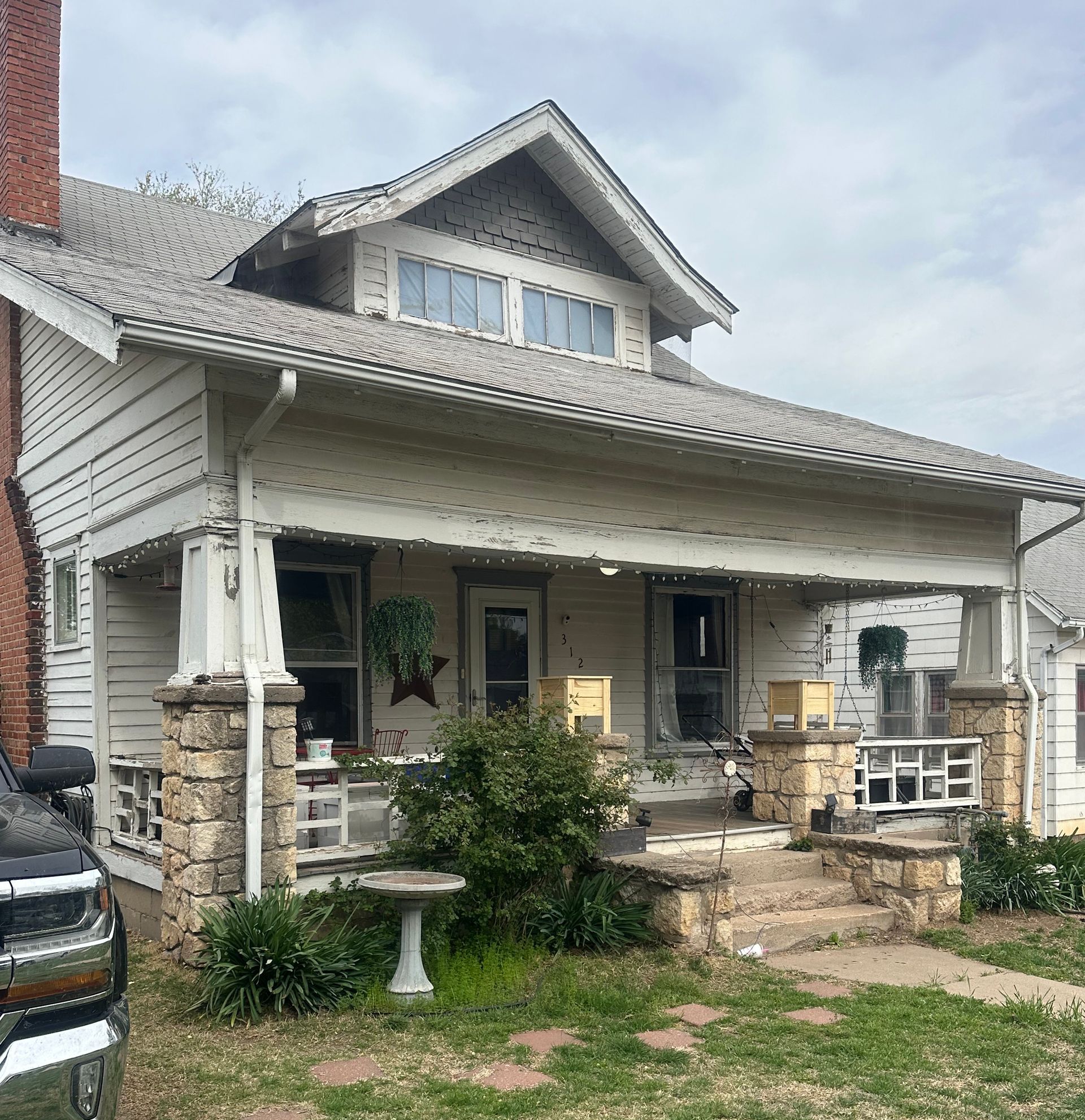 Two-story white house with stone columns and porch, brick chimney, and a black SUV.