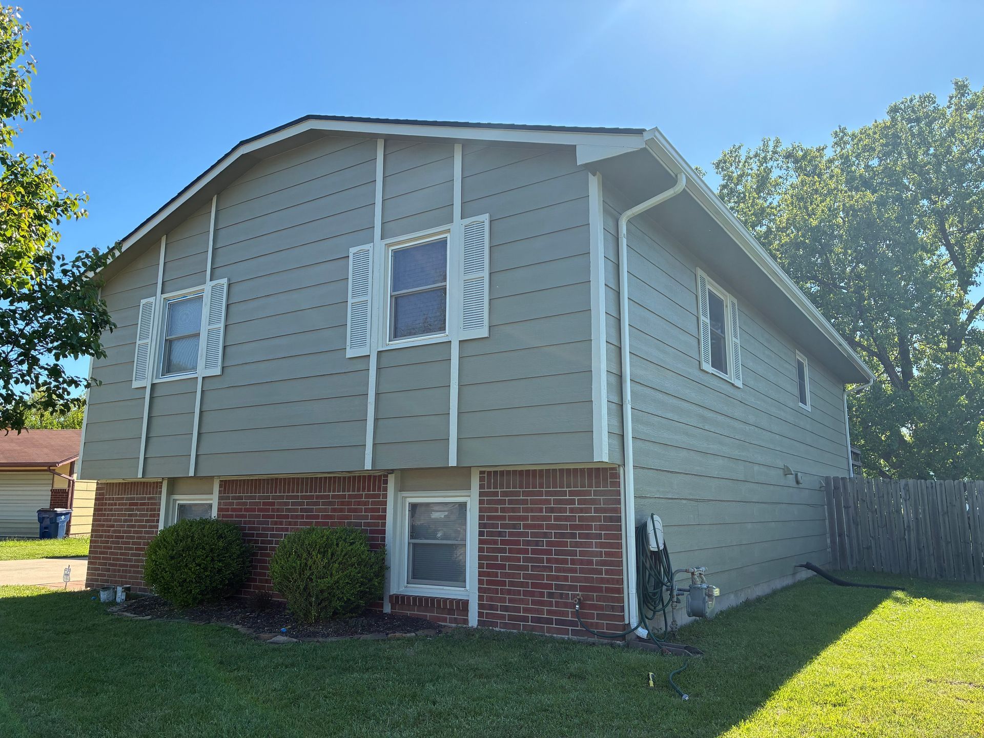 Two-story house with gray siding, red brick base, white shutters, and a green lawn.