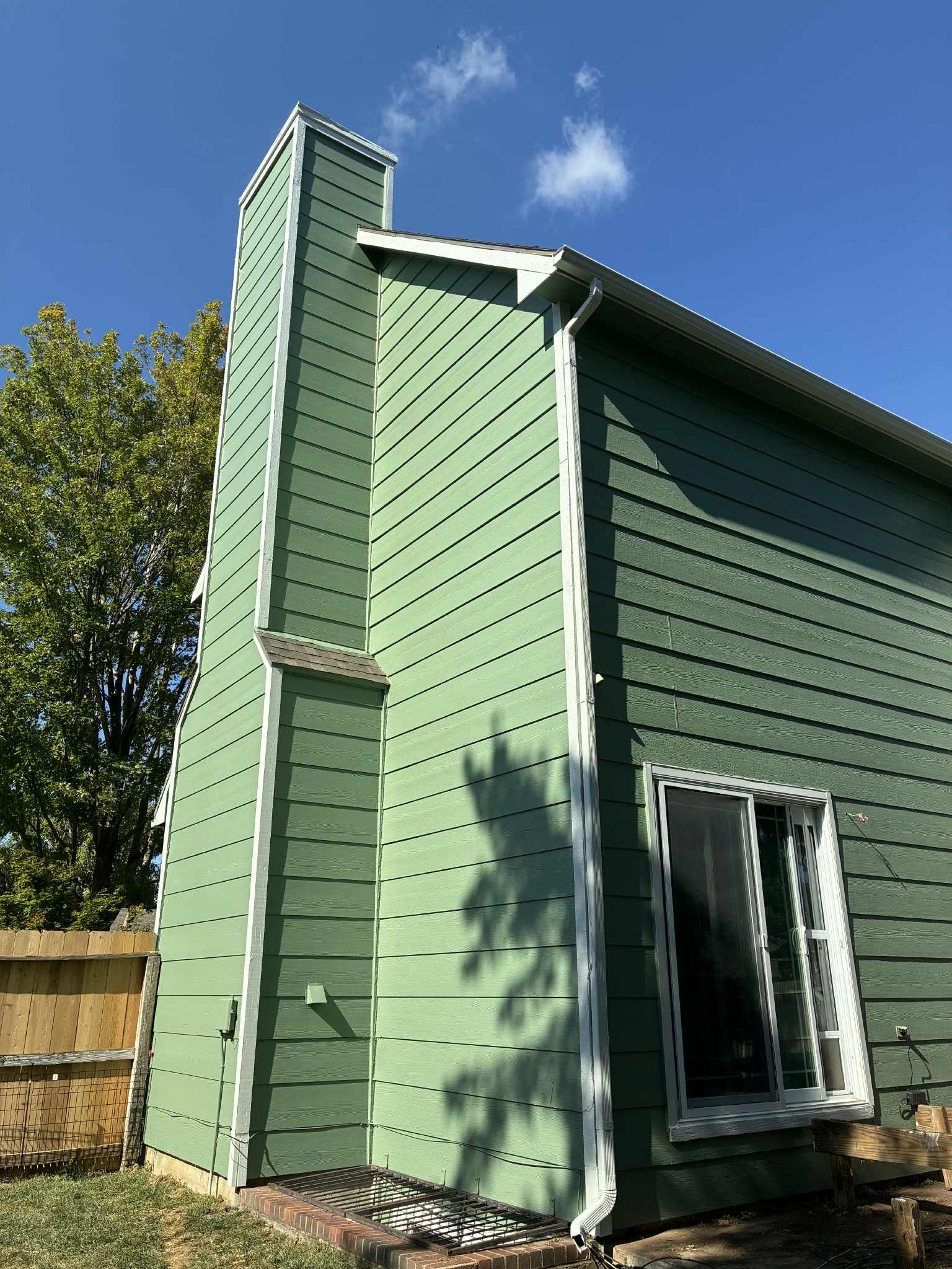 Green siding of a house with a tall chimney and white trim against a blue sky.