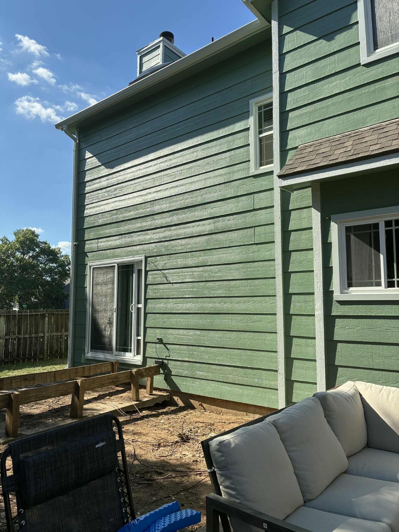 Green-sided house with white trim and windows, a partially built deck, and outdoor furniture.