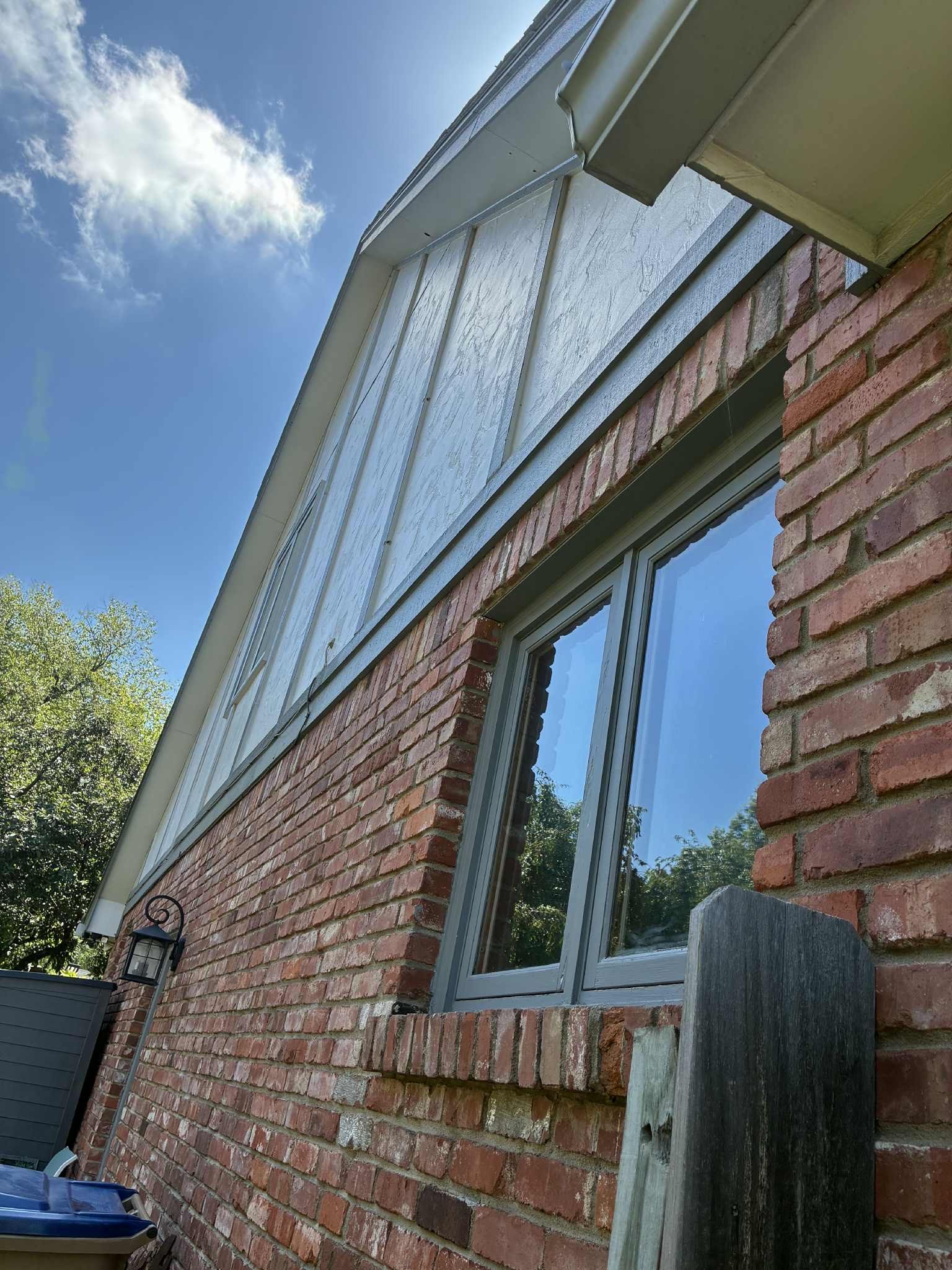 Brick house exterior with a window and metal siding under a blue sky.