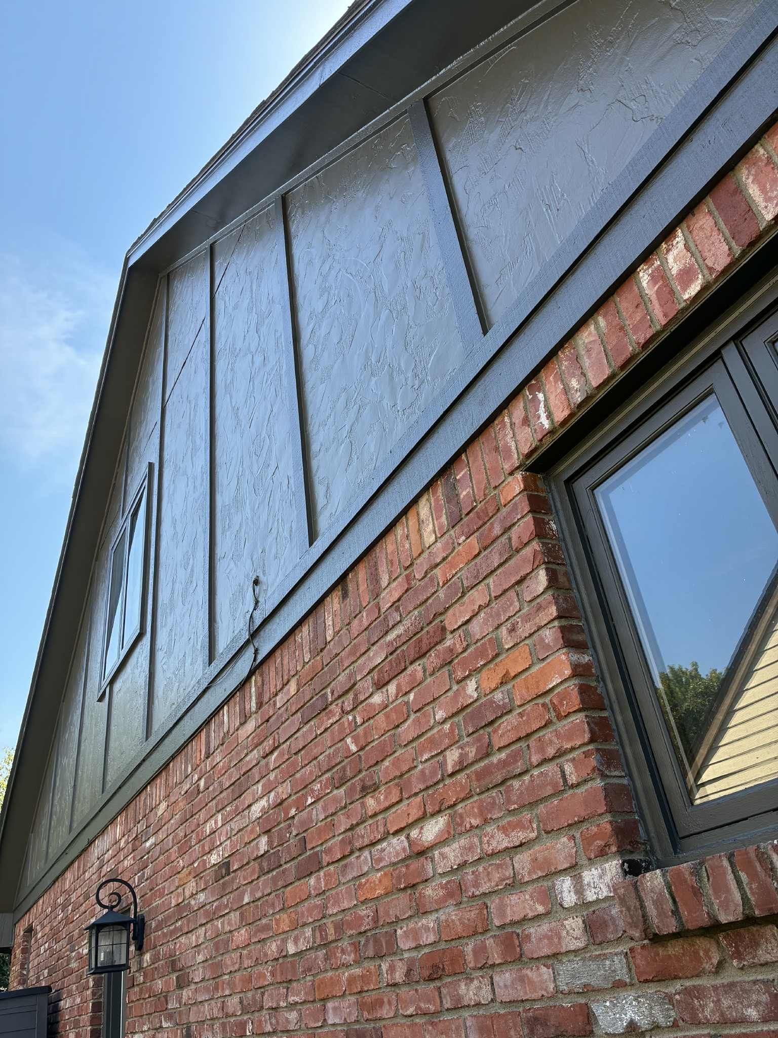 Brick house exterior with dark siding, black trim, and a window against a blue sky.