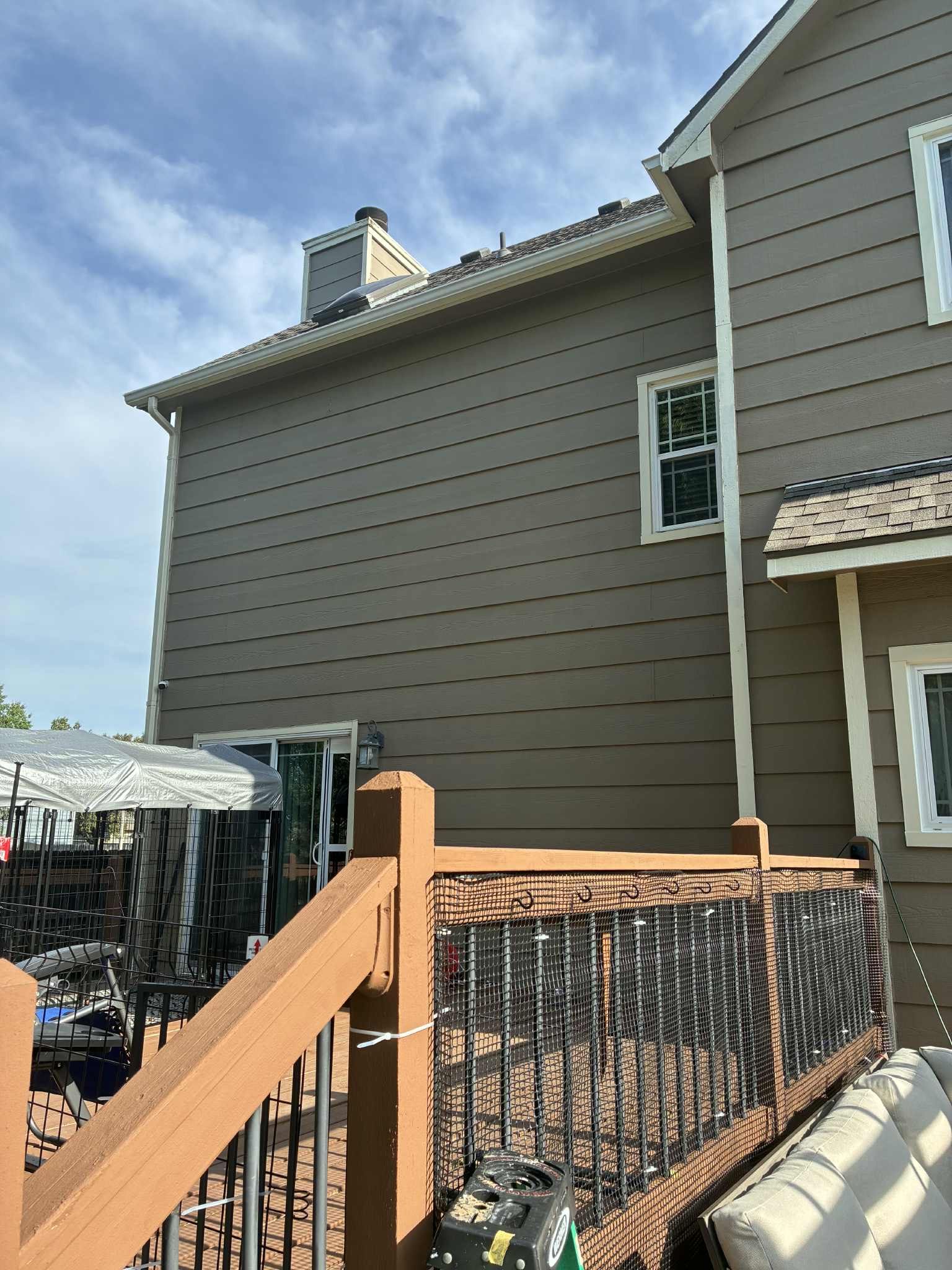 Side of a two-story beige house with a brown deck, chimney, and a cloudy sky.