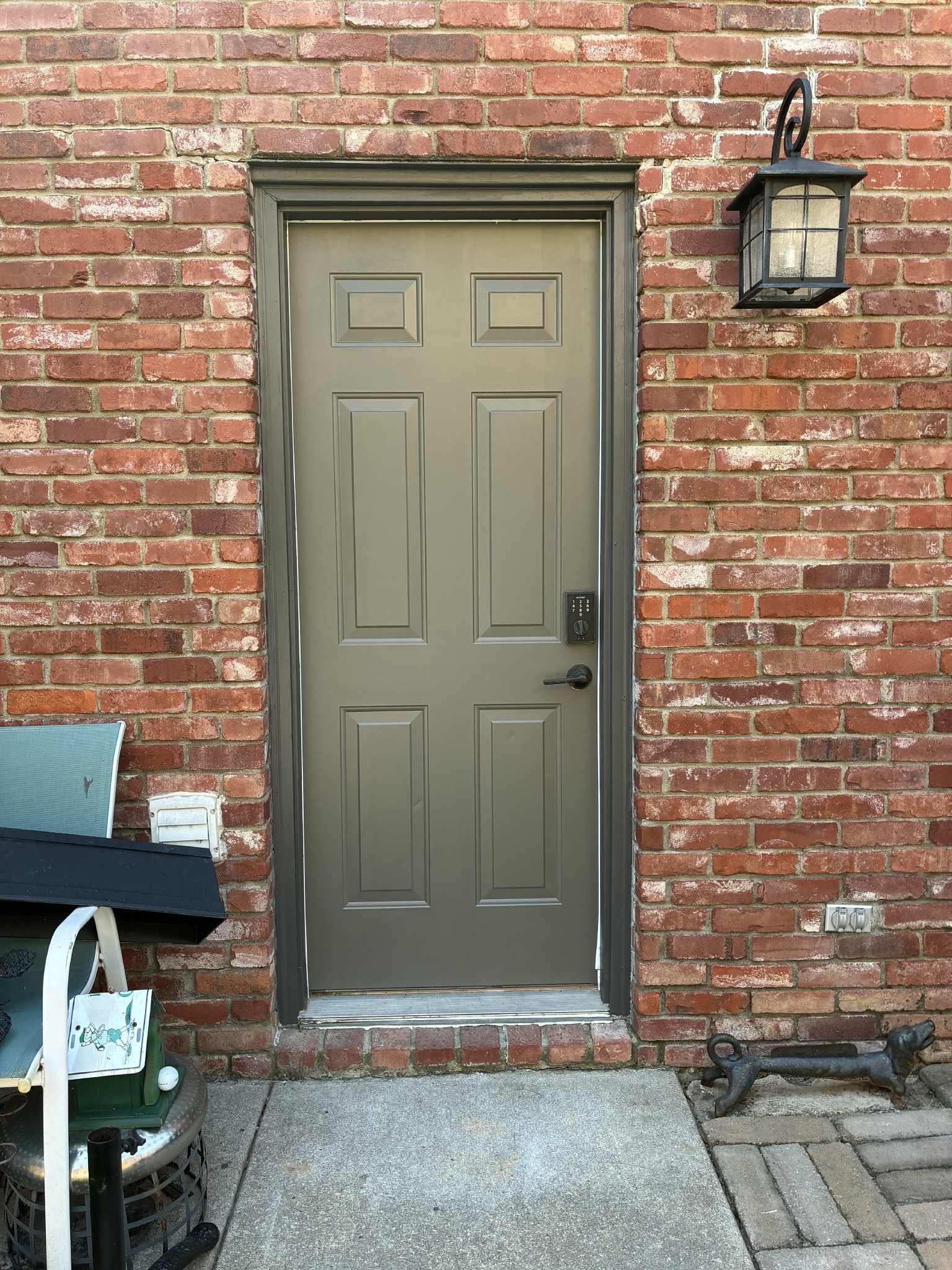A brown door with gray trim on a brick building, with a lantern and walkway.