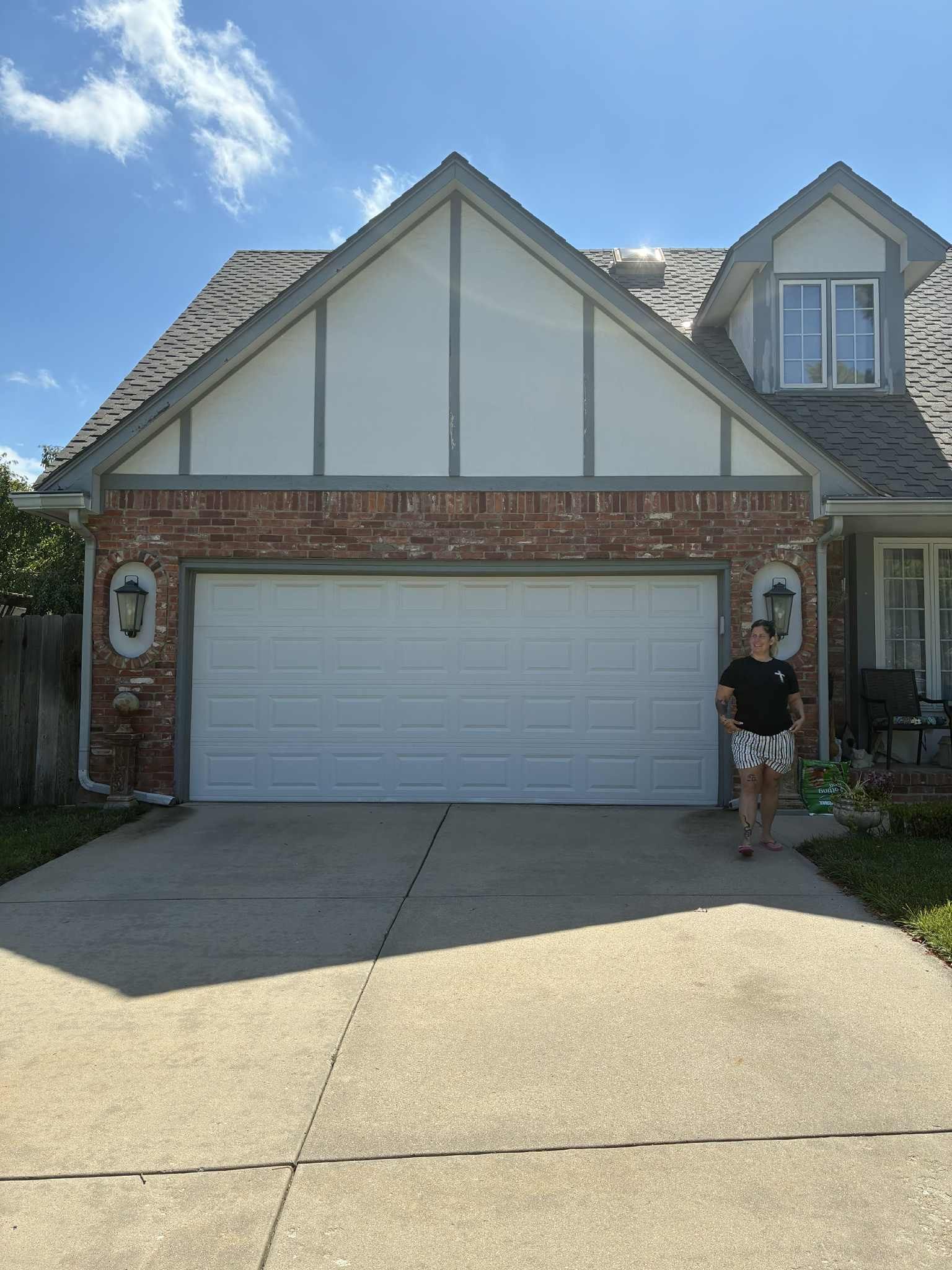 A person stands in front of a two-car garage with a red brick facade under a clear blue sky.