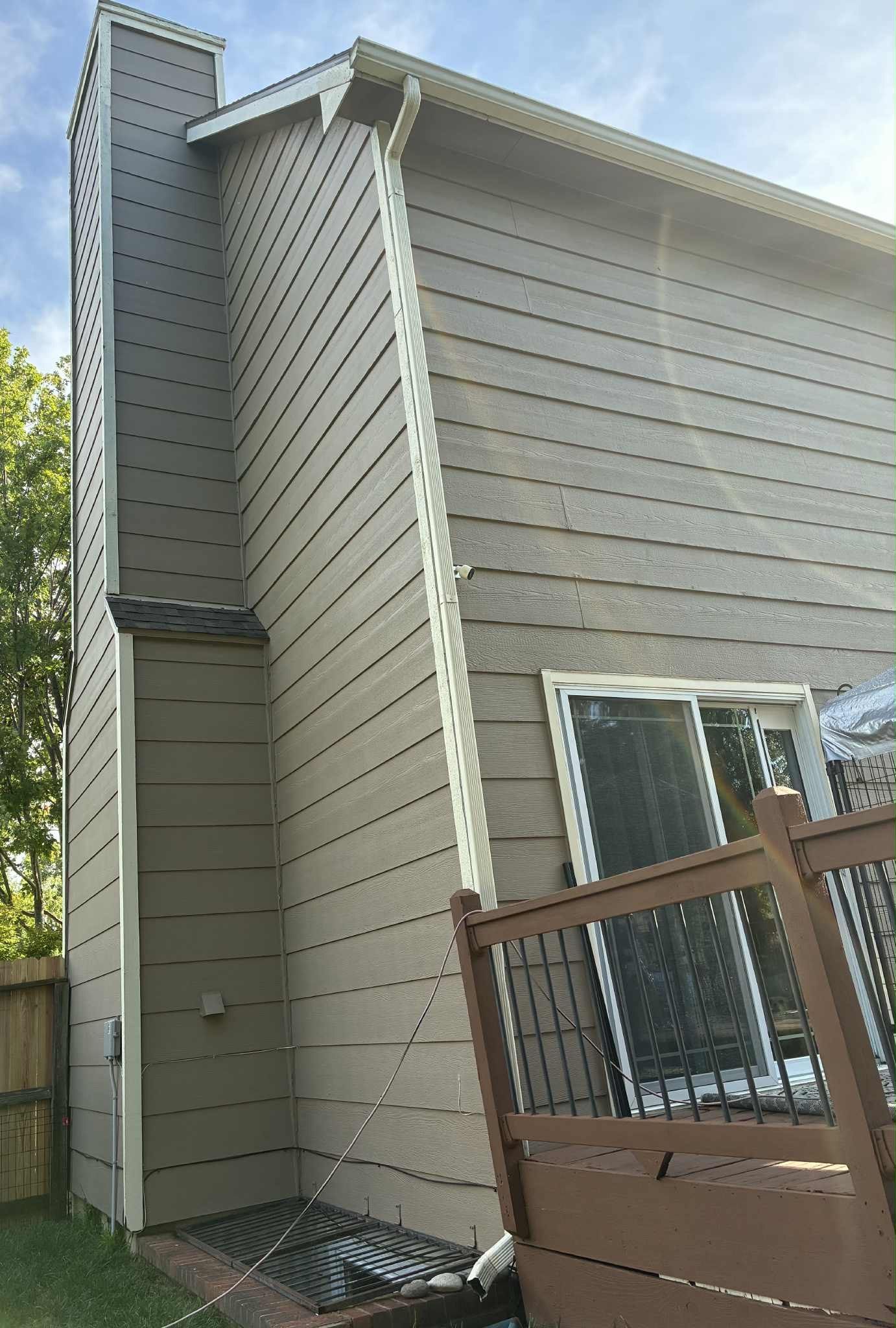 Side view of a two-story house with a chimney, siding, a window, and a wooden deck.