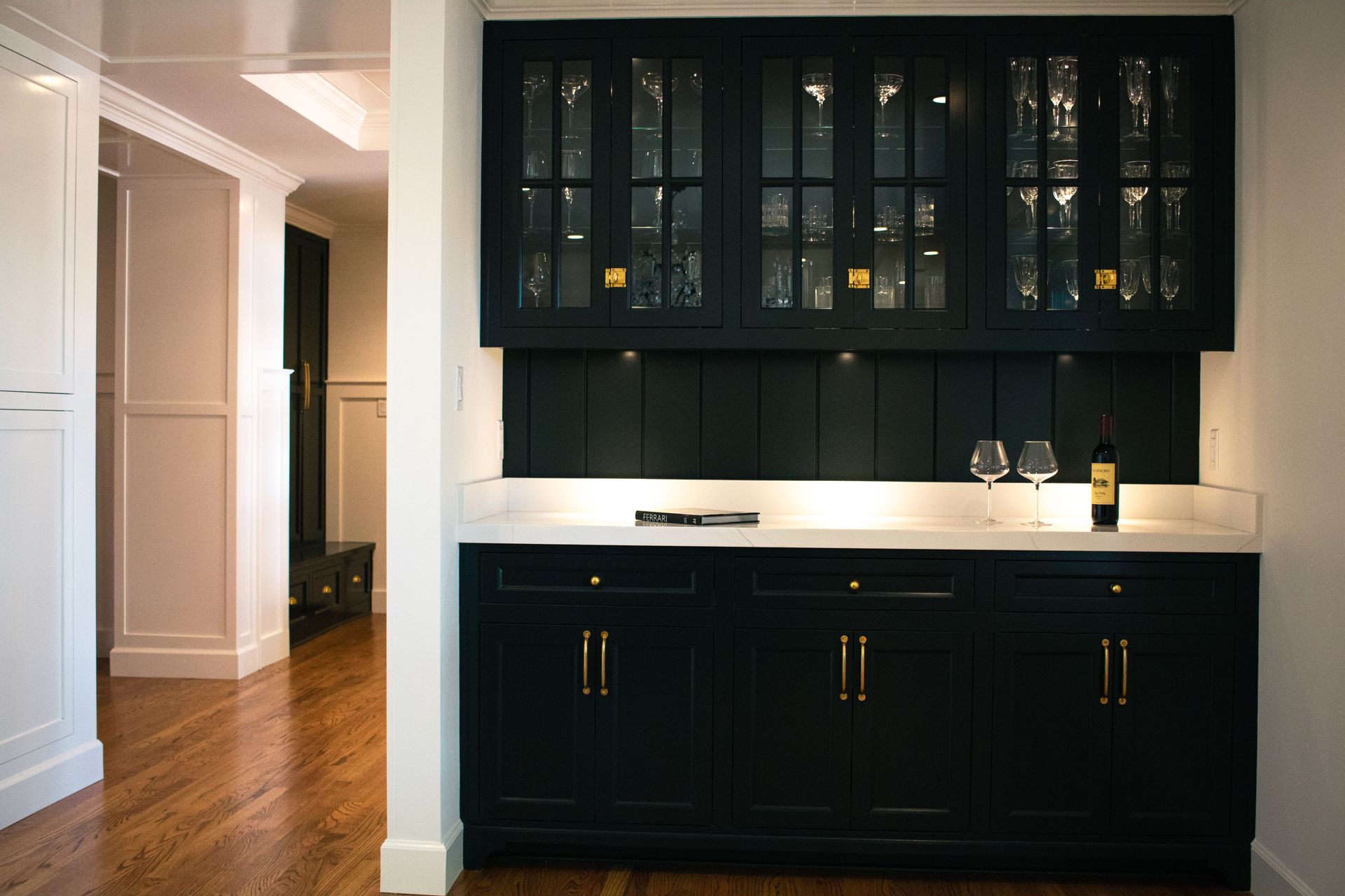 Dark blue built-in bar with glass-fronted cabinets, marble countertop, and wood floors.