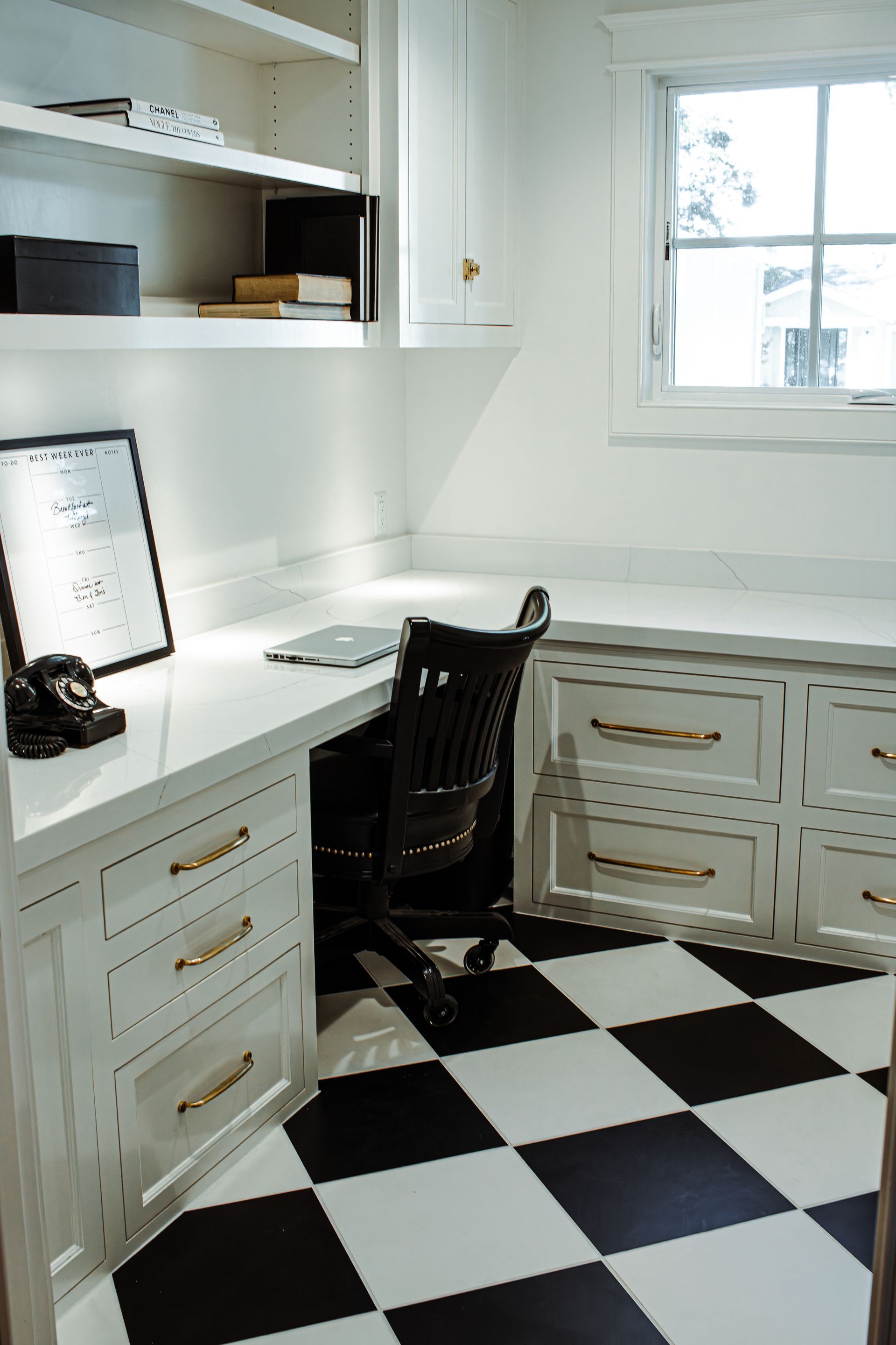 Office with white desk, cabinets, and black and white checkered floor. Includes black office chair and window.