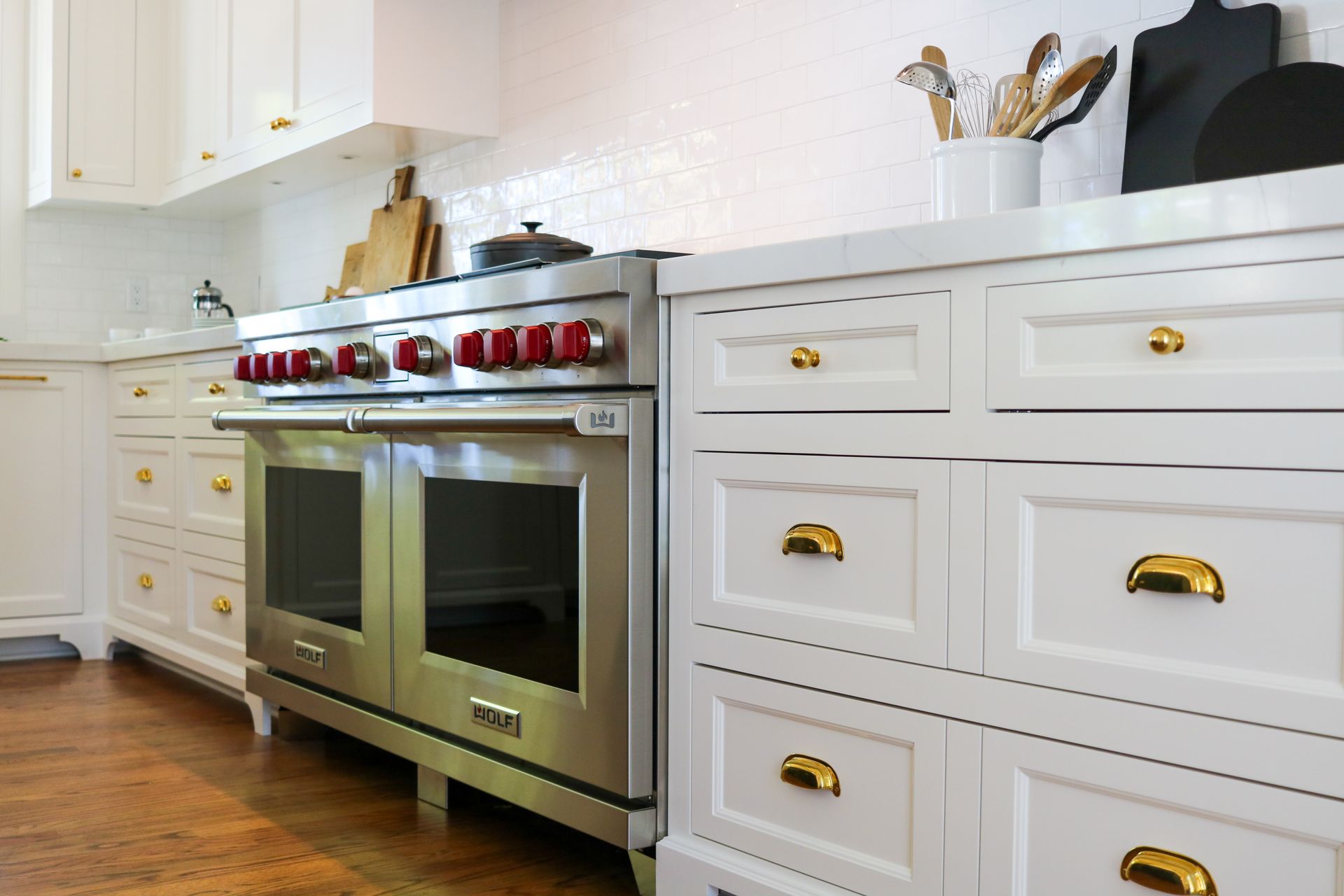 Modern kitchen with white cabinets, stainless steel range, and gold hardware.