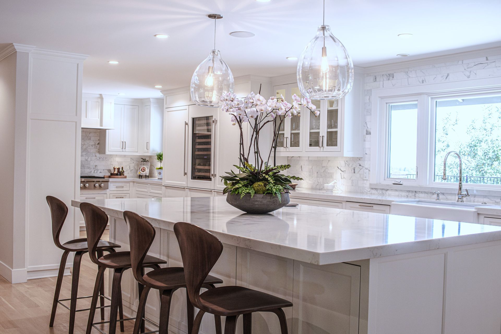 White kitchen with island, pendant lights, wooden stools, and floral arrangement.
