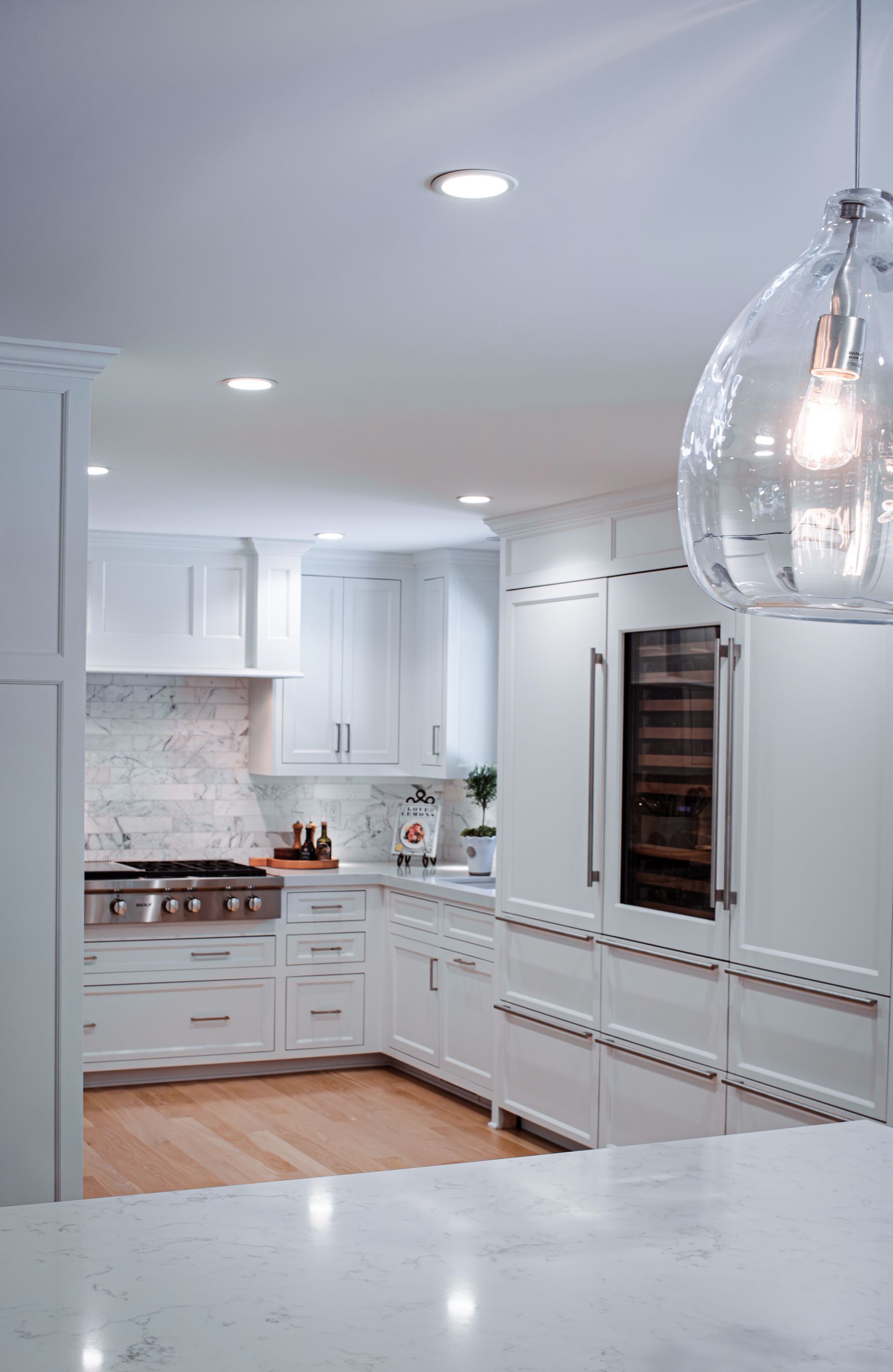 White kitchen with cabinets, stainless steel appliances, and a glass pendant light.