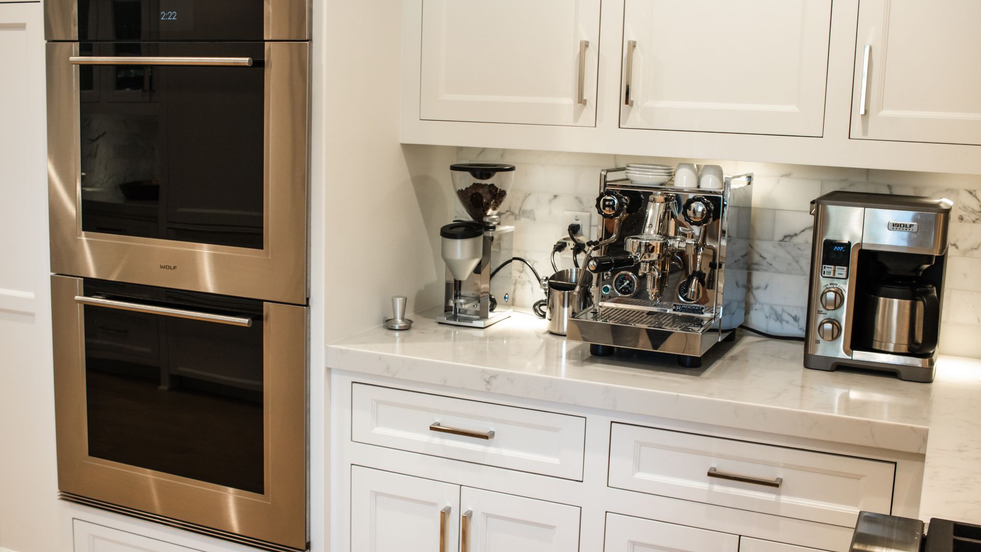 Built-in ovens and coffee station with espresso machine, grinder, and coffee maker on a white countertop.