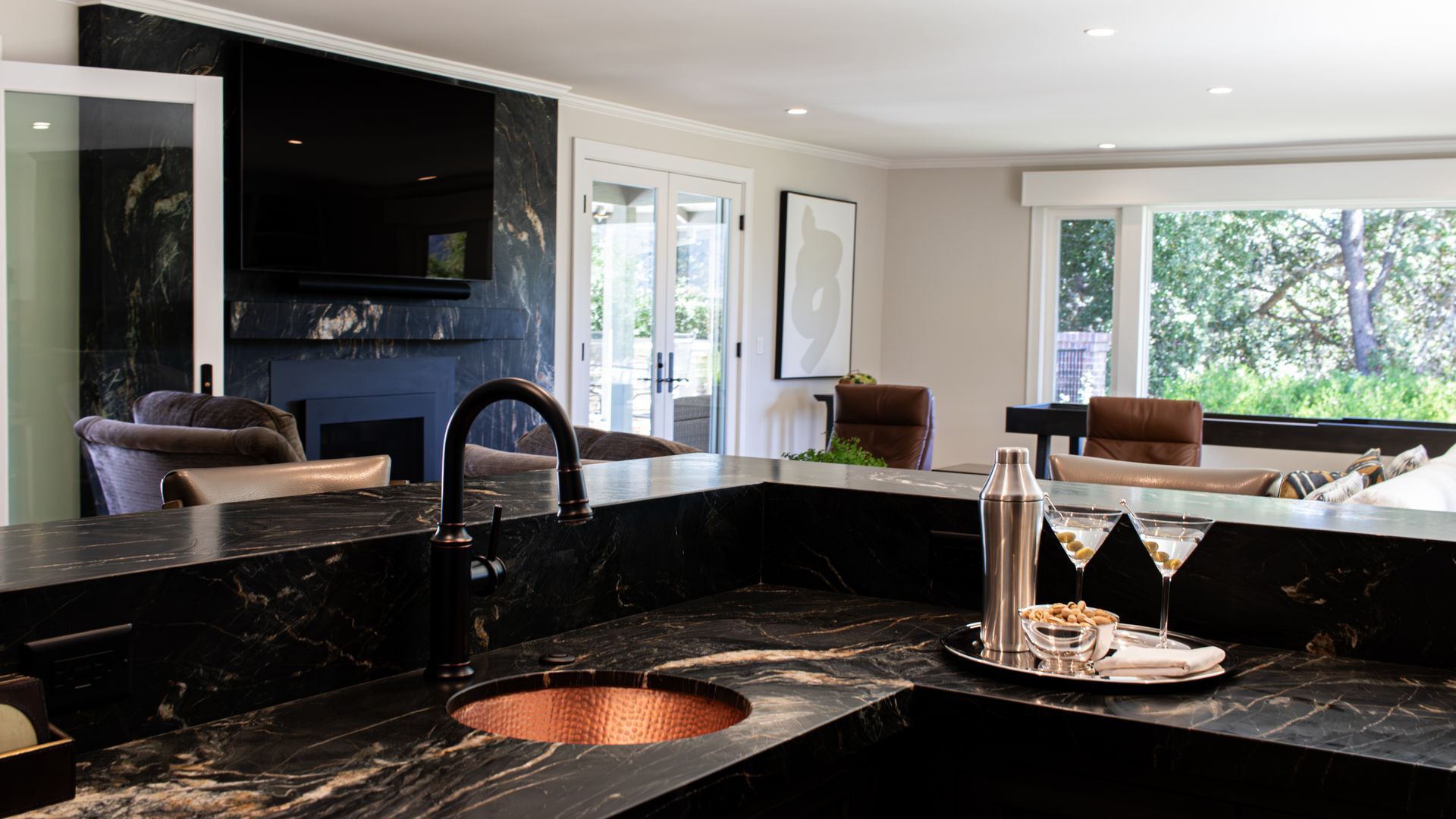 Kitchen with black countertop, copper sink, and martini set; a television is mounted on a black wall.