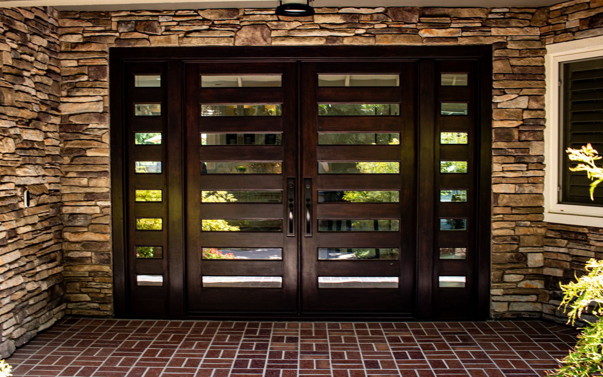 Dark wooden double front doors with rectangular glass panels, set in a stone wall.