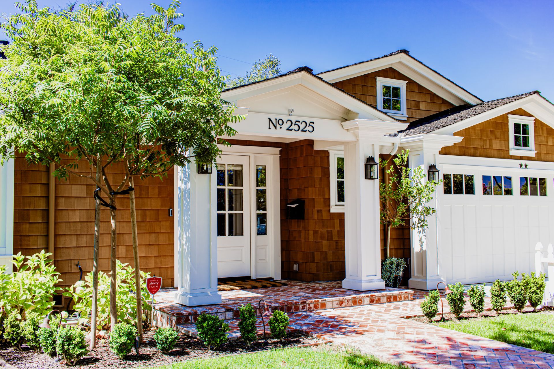 Charming two-story house with brown shingle siding, white trim, and a brick walkway.