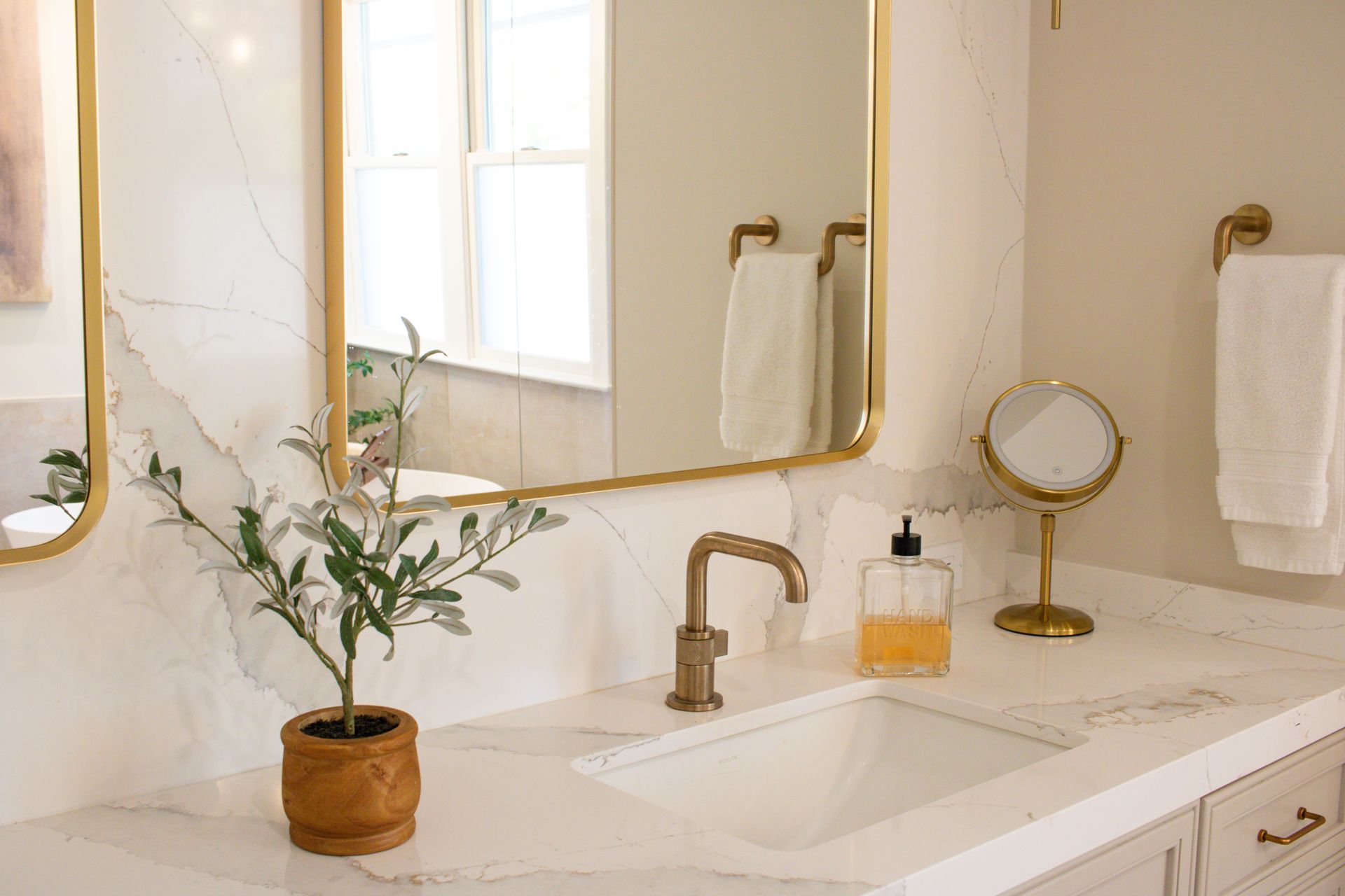 Bathroom with gold accents, marble countertops, and a potted plant by the sink.