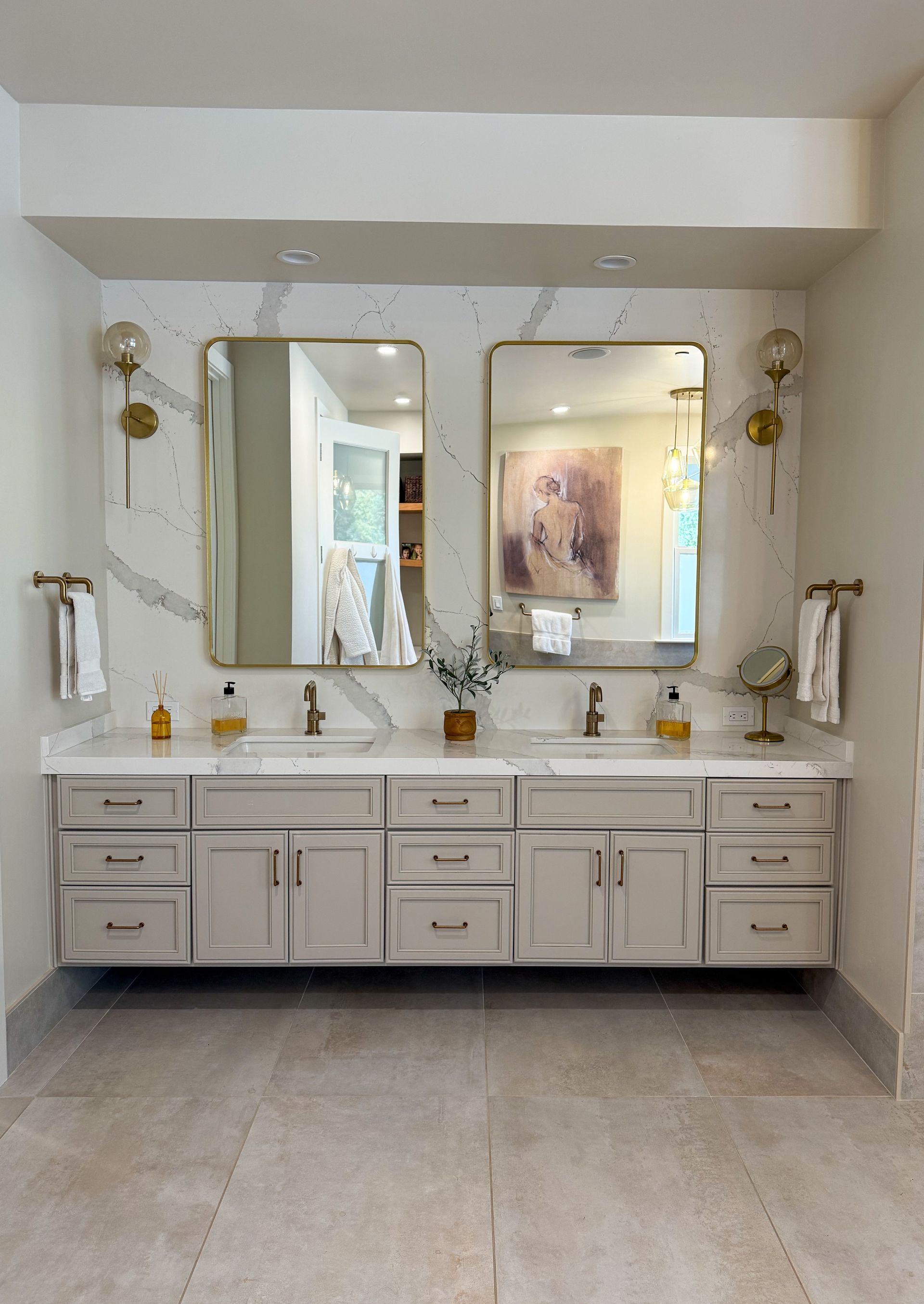 Modern bathroom with a double vanity, marble backsplash, and gold-framed mirrors.