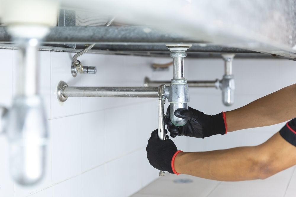 Plumber With Black Gloves Works Under a Sink — Oxplumb in Coolum Beach, QLD