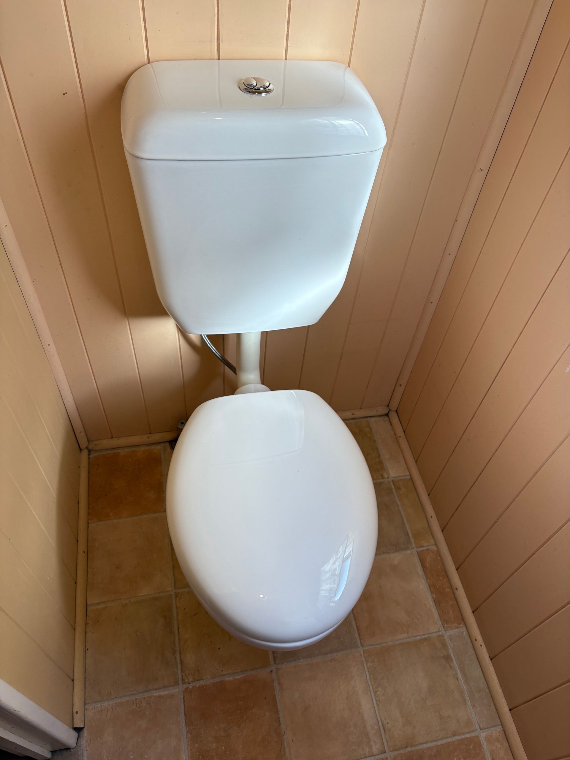 White Toilet With Lid, in Small Room With Beige Walls and Tiled Floor — Oxplumb in Maroochydore, QLD