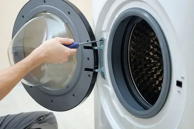 A Person Uses a Screwdriver to Repair the Washing Machine Door — Central Coast Washing Machines & Refrigerator Repairs in Gosford, NSW