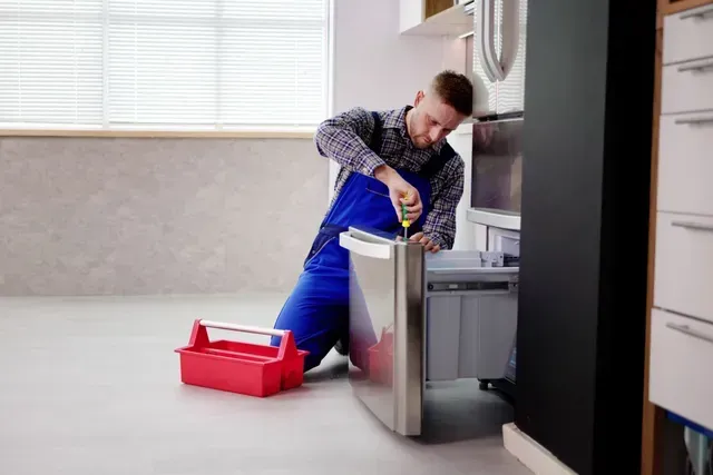 A Technician Using a Screwdriver to Repair a Stainless Steel Dishwasher — Central Coast Washing Machines & Refrigerator Repairs in Gosford, NSW