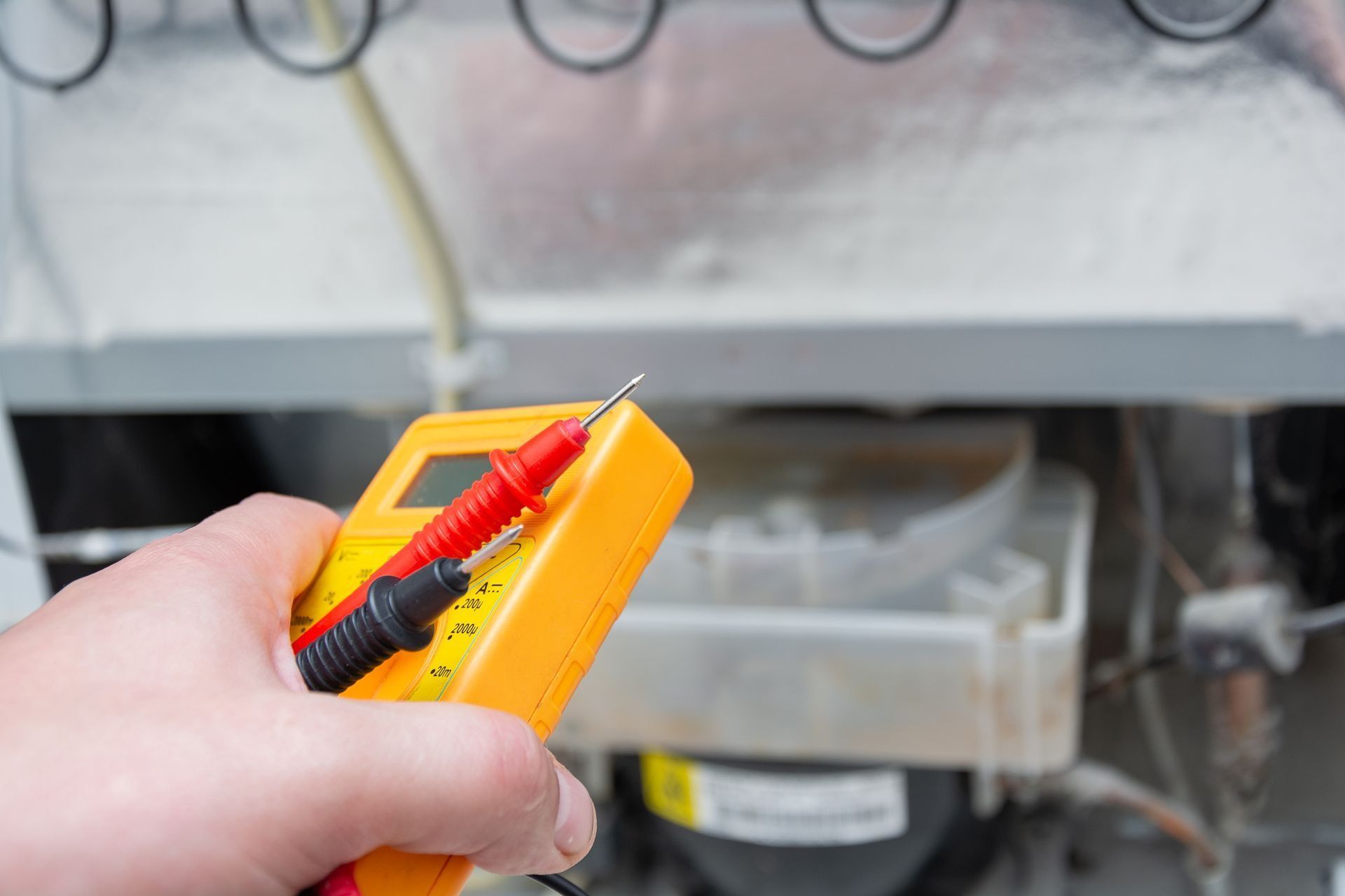 A Person Holds a Multimeter While Inspecting the Back of an Appliance — Central Coast Washing Machines & Refrigerator Repairs in San Remo, NSW