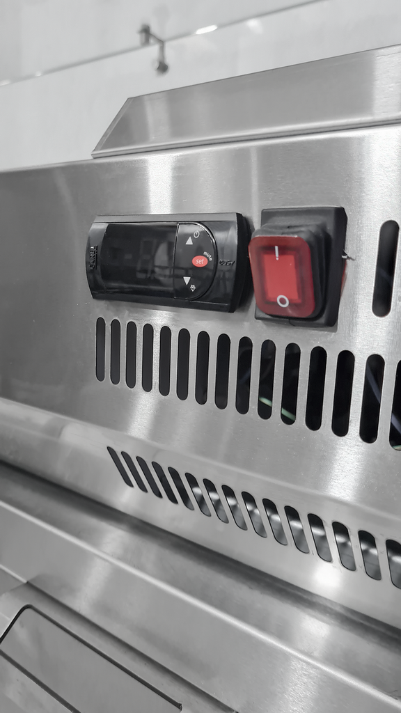 Vitrina refrigerada de acero inoxidable con tapa de cristal. Contiene varios recipientes para alimentos.