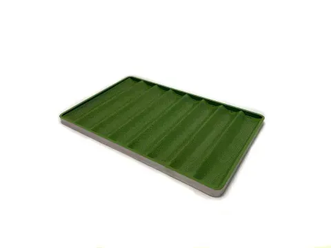 Molde para hornear baguette con seis canales, fabricado en metal, ligeramente inclinado sobre una superficie blanca.
