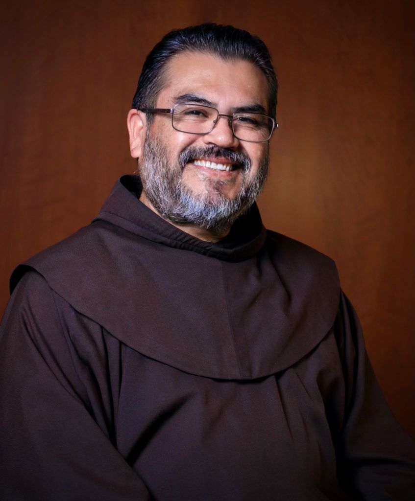 A man with glasses and a beard is wearing a brown robe