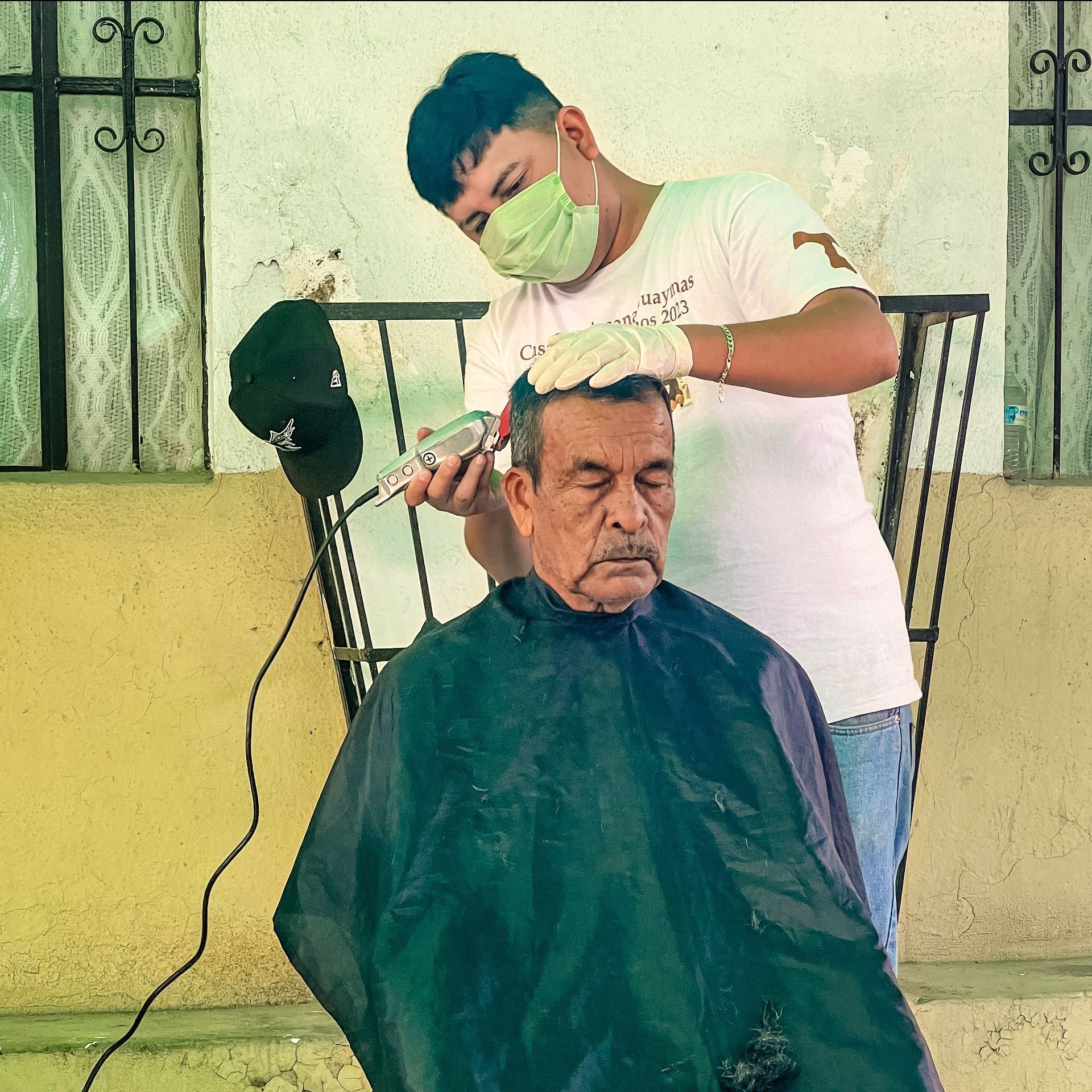 An older man is getting his hair cut by a man wearing a mask