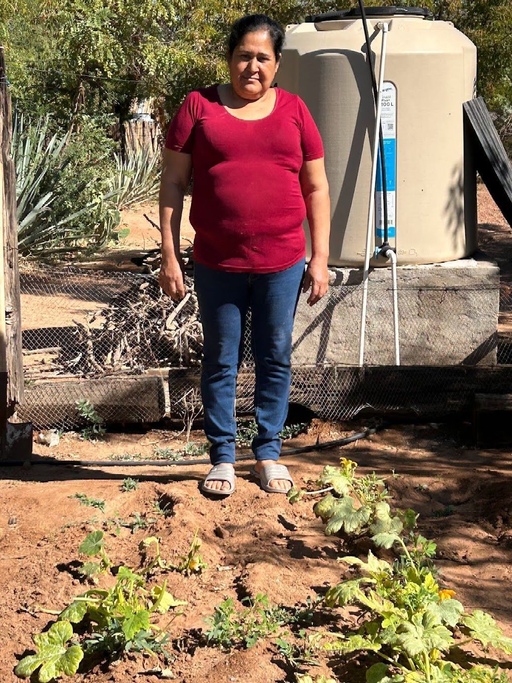 A woman is standing in front of a water tank in a garden.