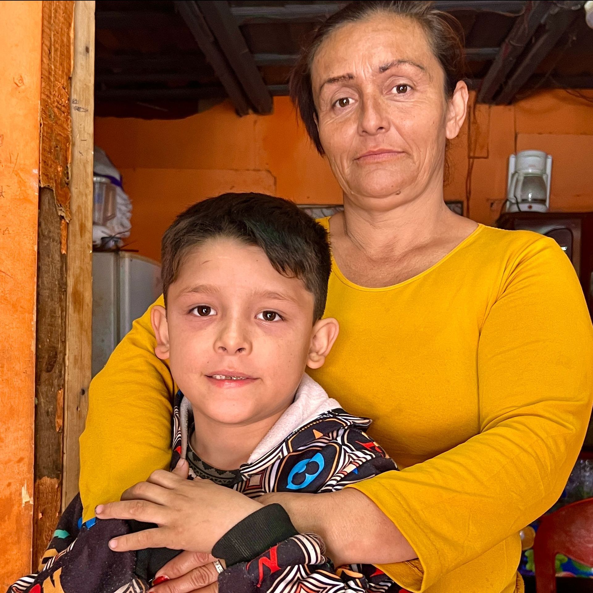 A woman in a yellow shirt is hugging a young boy