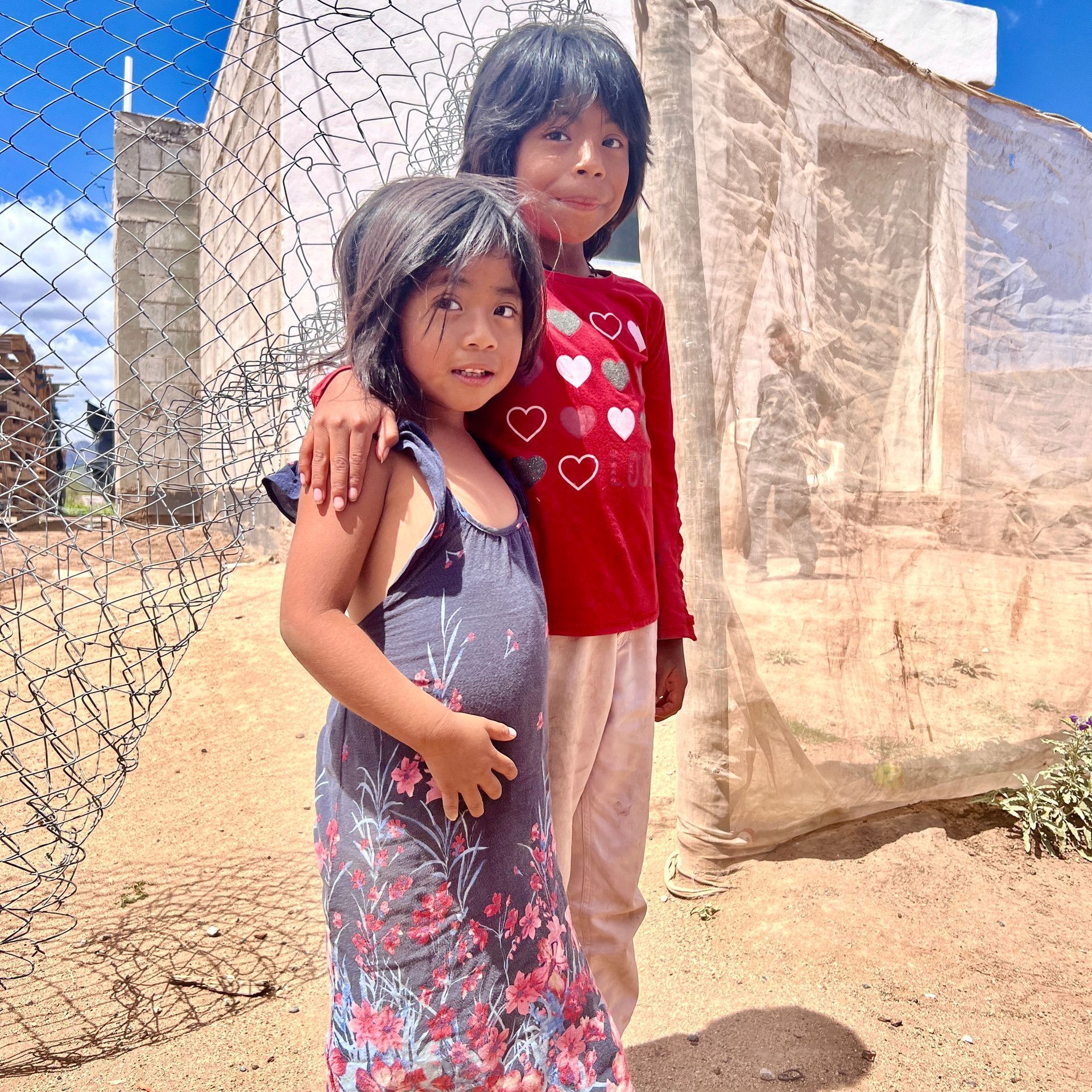Two little girls standing next to each other in front of a chain link fence