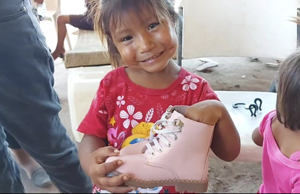 A little girl in a red shirt is holding a pink shoe.