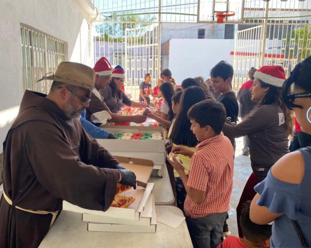 A man in a brown robe is serving pizza to a group of people