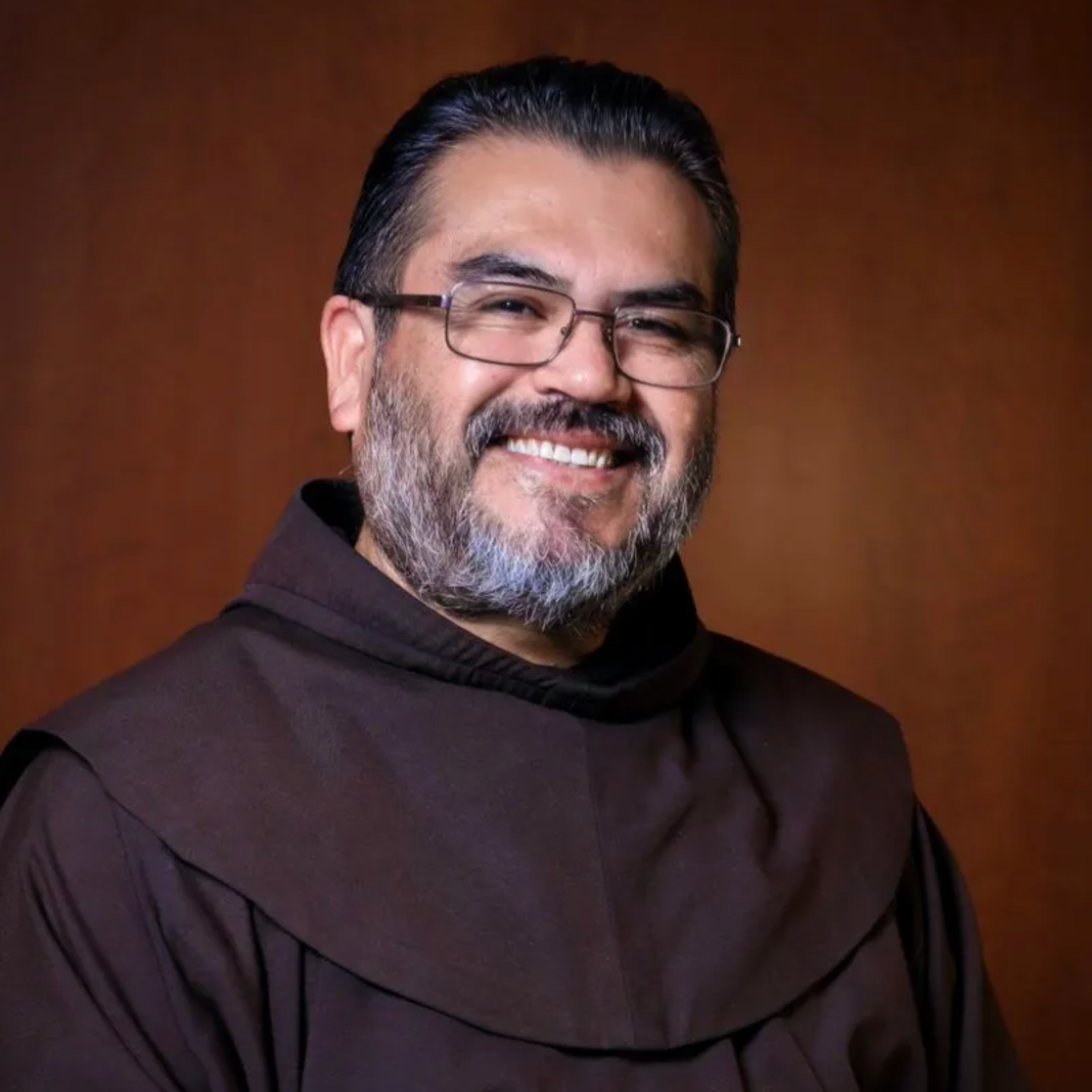 A man with glasses and a beard is wearing a brown robe