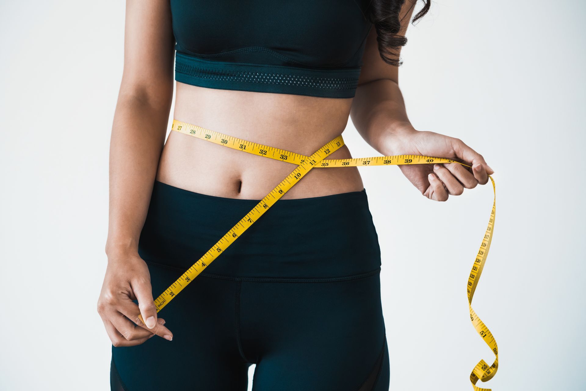 Person measuring waist with a tape measure, tracking fitness progress, weight loss goals.
