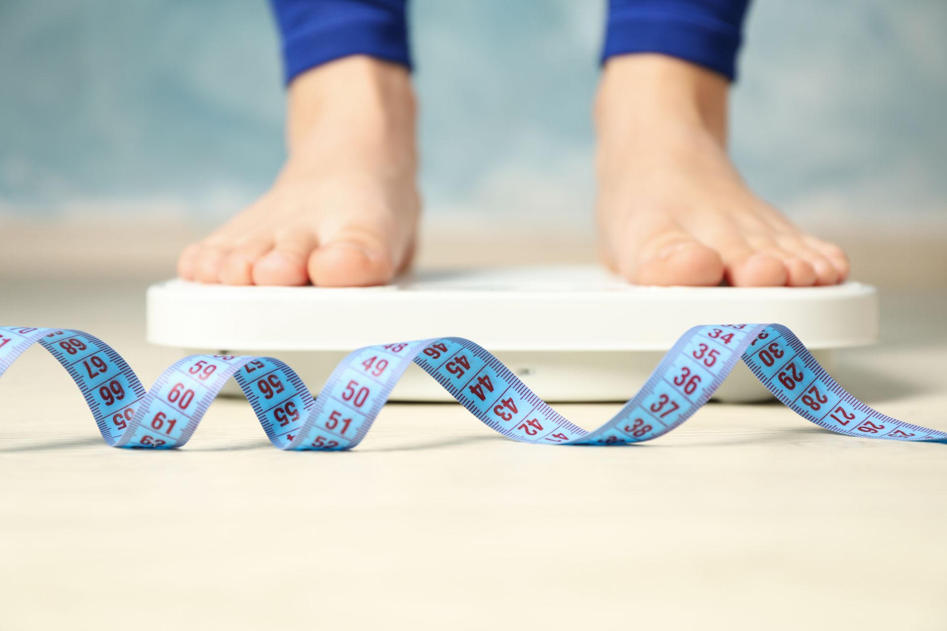 Person standing barefoot on a bathroom scale with measuring tape nearby.