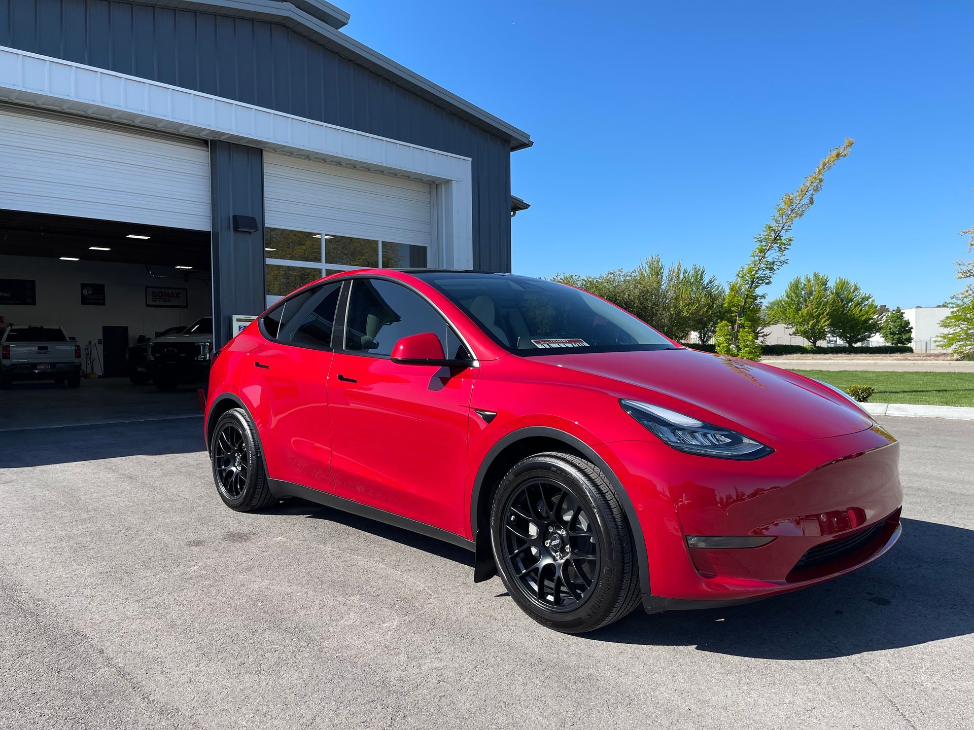 A red tesla model y is parked in front of a garage.