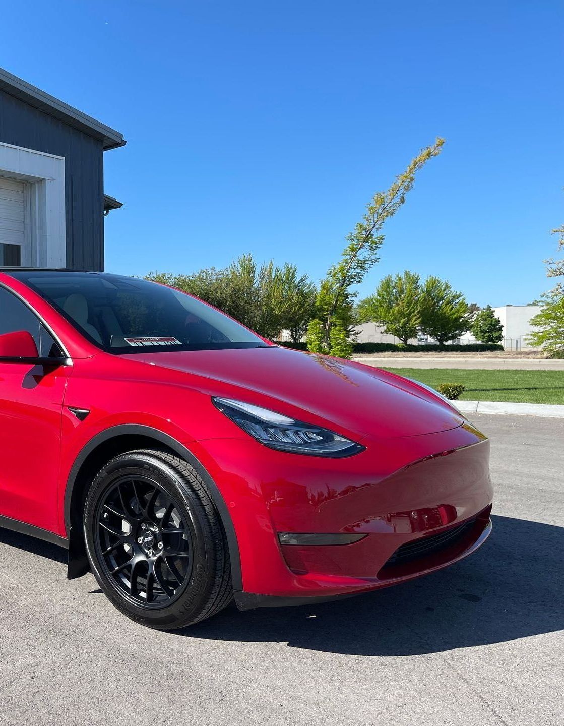A red tesla model y is parked in front of a garage.