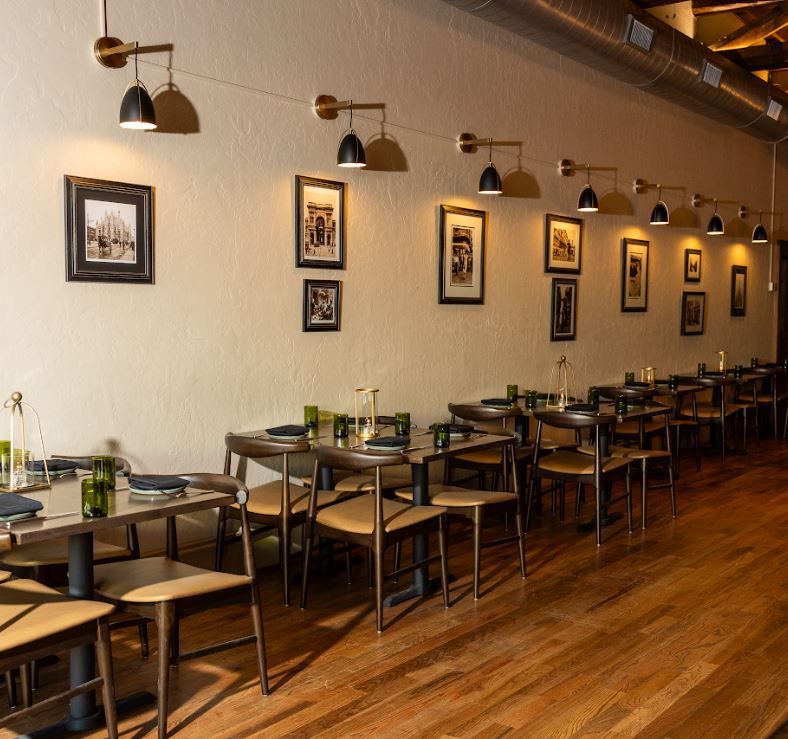 Modern restaurant dining room with neatly set tables, framed wall art, and warm pendant lighting.