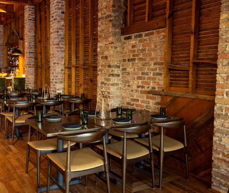 Empty restaurant dining area with wooden tables, metal chairs, and brick-and-wood walls