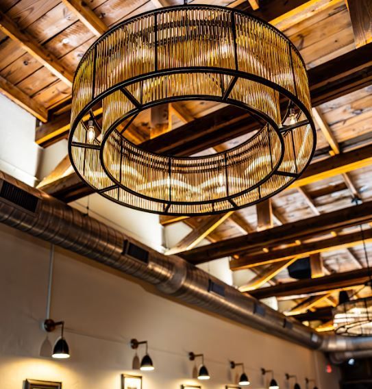 Rustic ceiling with woven ring chandelier and exposed wooden beams in a warmly lit interior
