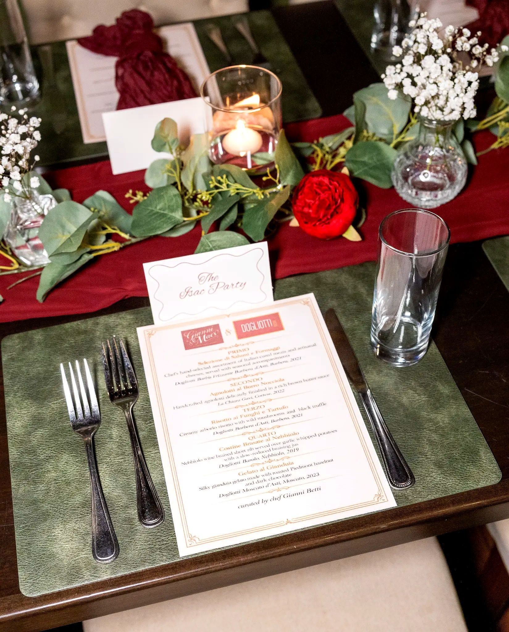 Elegant table setting with red and green floral centerpiece, candle, menu, and silverware on a dark tablecloth